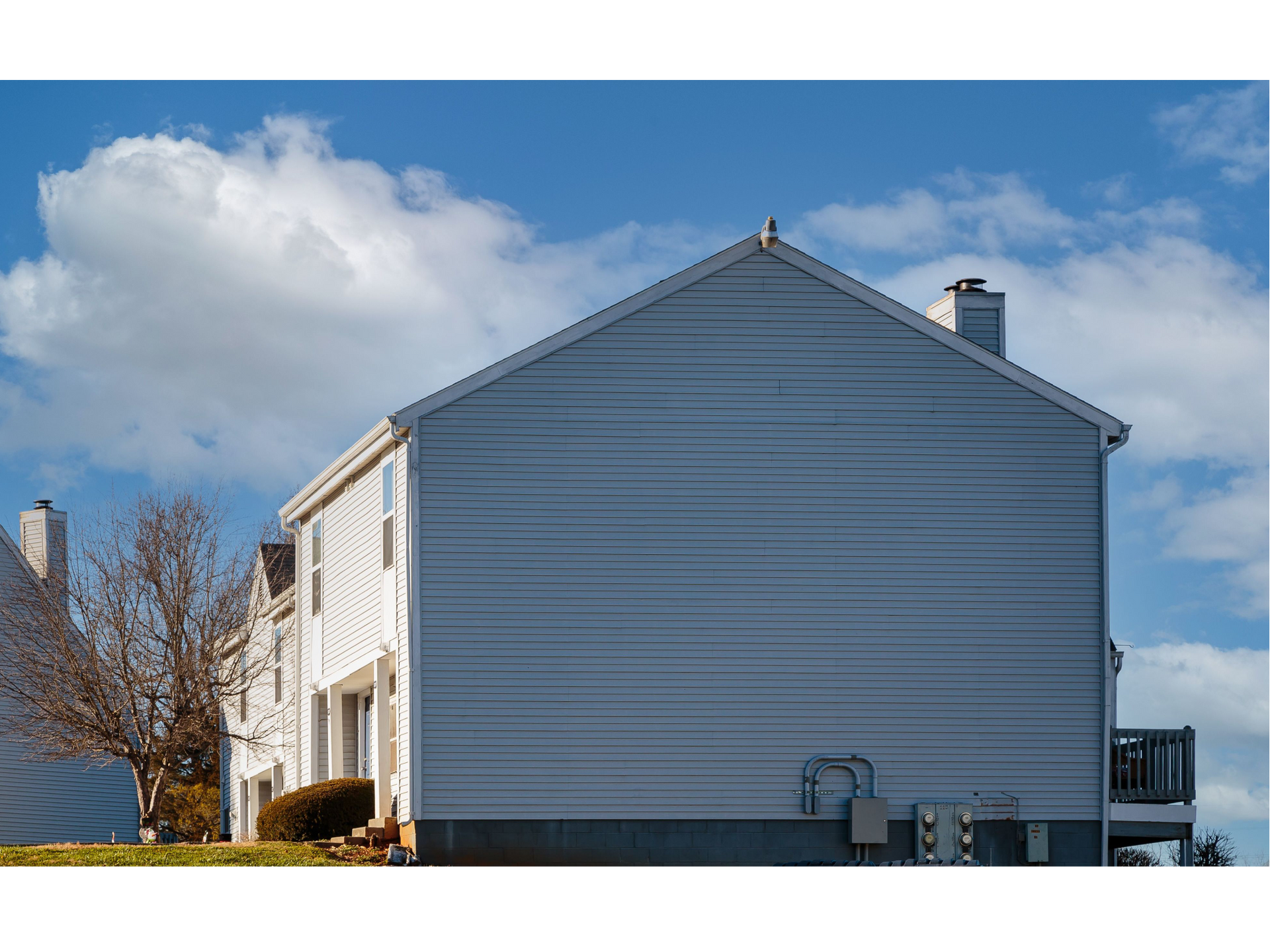 Side view of a light gray two-story house with a white porch under a blue sky