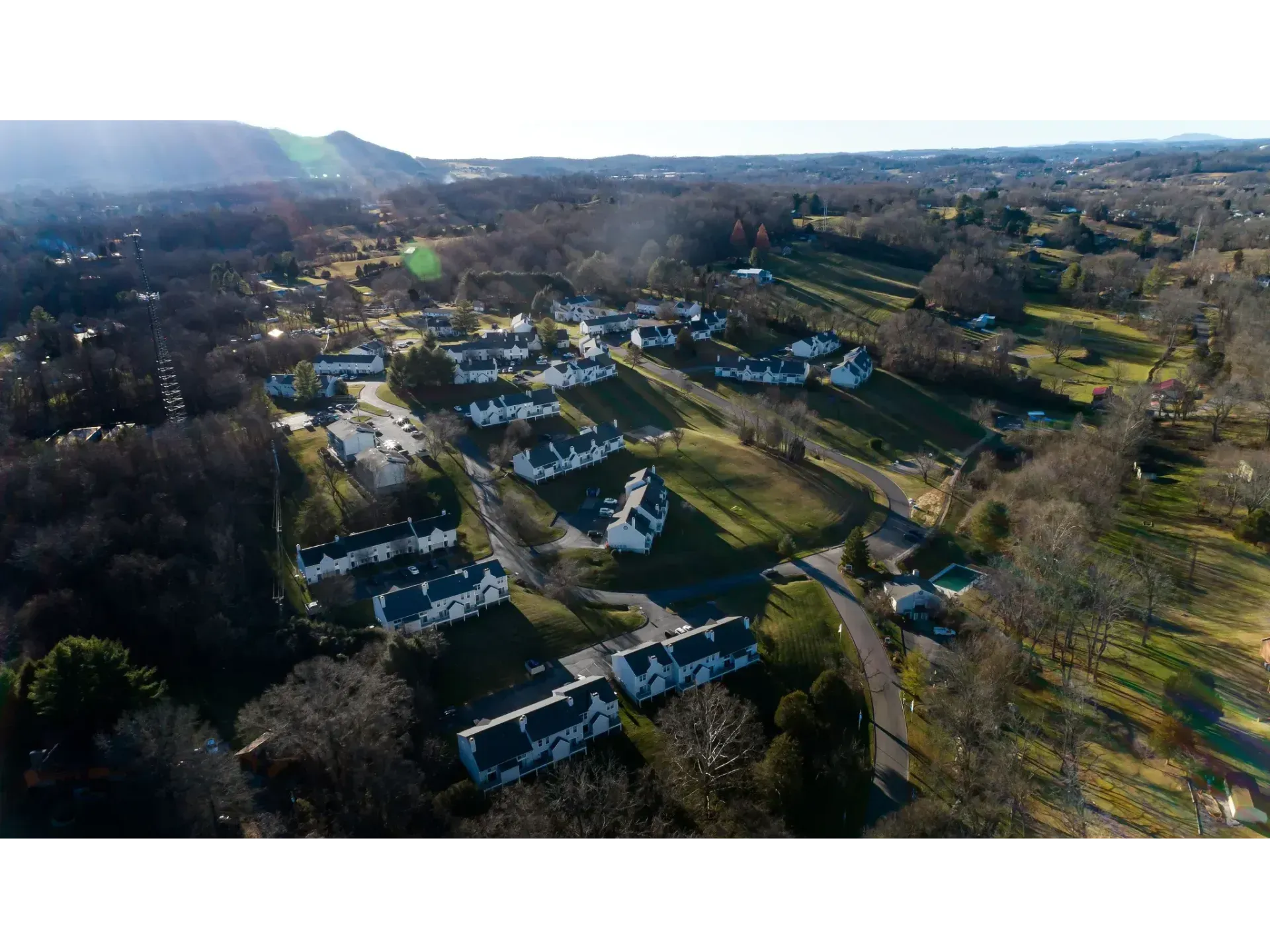 Aerial view of a residential neighborhood with rows of houses, trees, and sunlit roads.