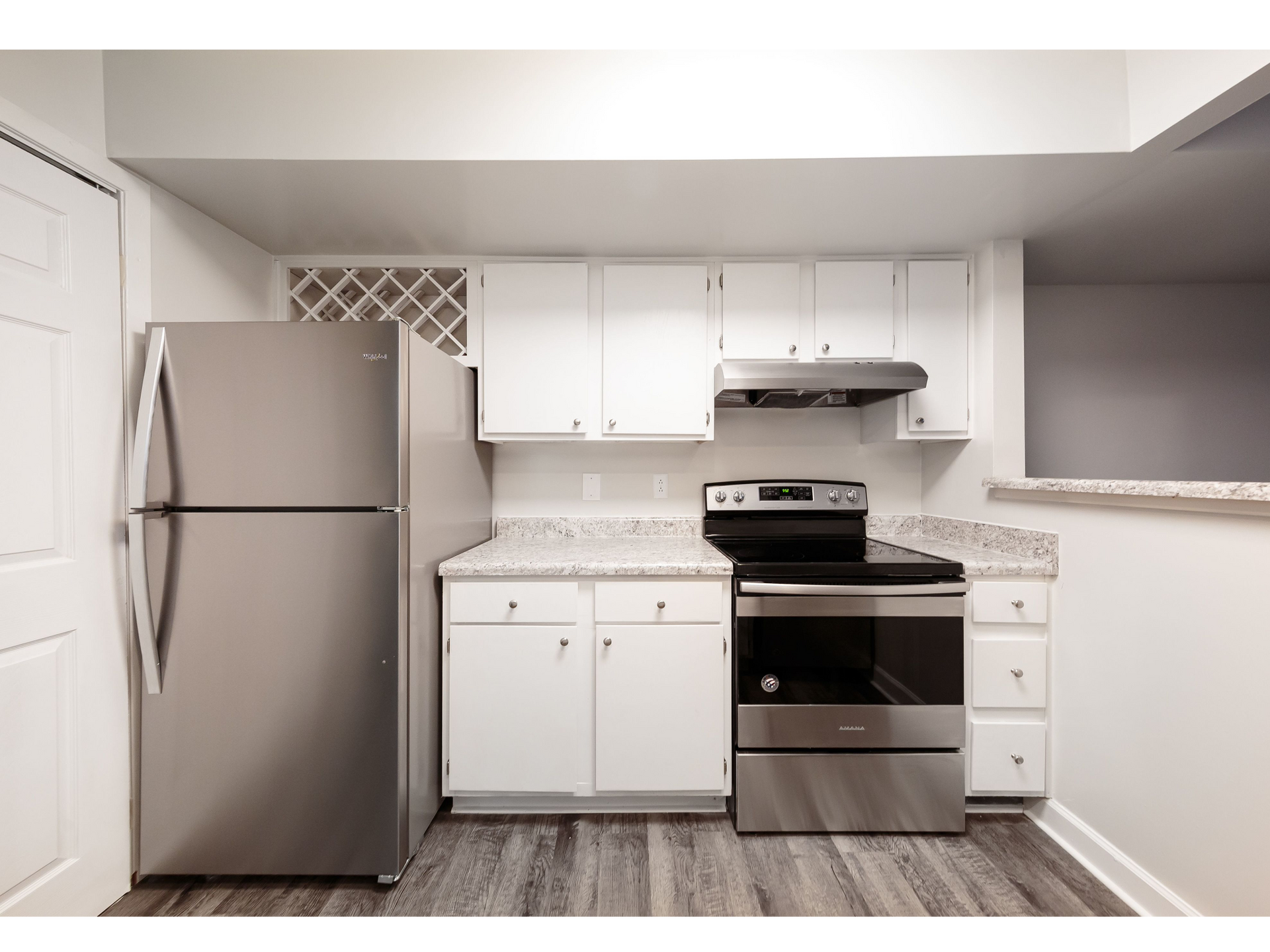 Compact kitchen with stainless steel appliances, white cabinets, and granite countertops