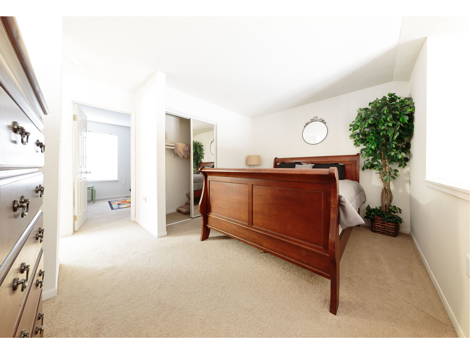 Bright bedroom with wooden bed, white walls, and a doorway to an adjoining bathroom