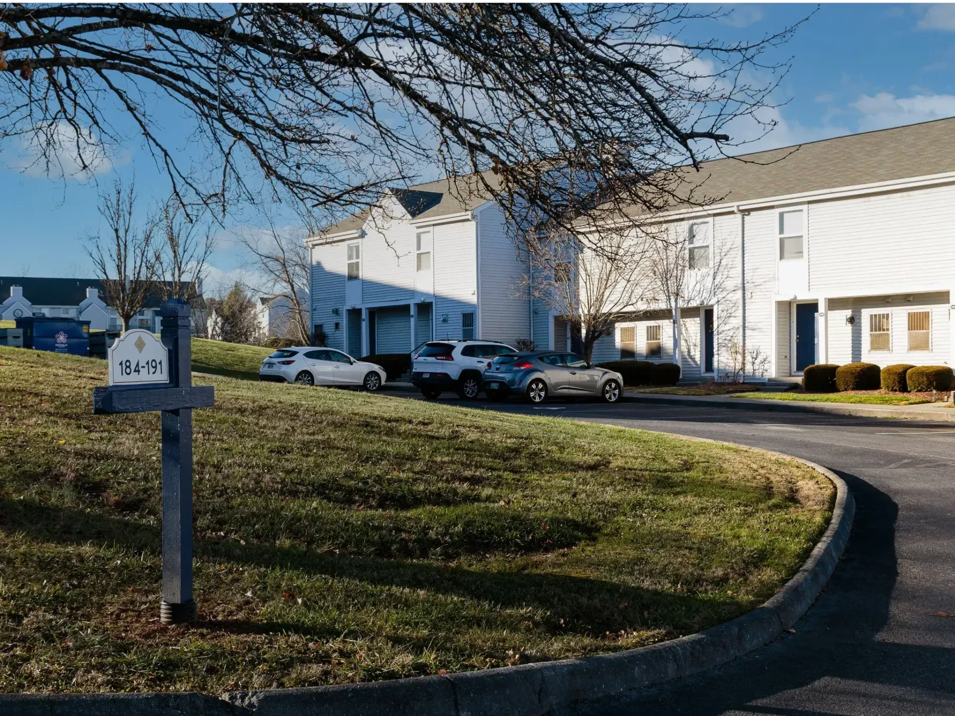 Apartment complex parking lot with white buildings, a mailbox, and parked cars on a sunny day