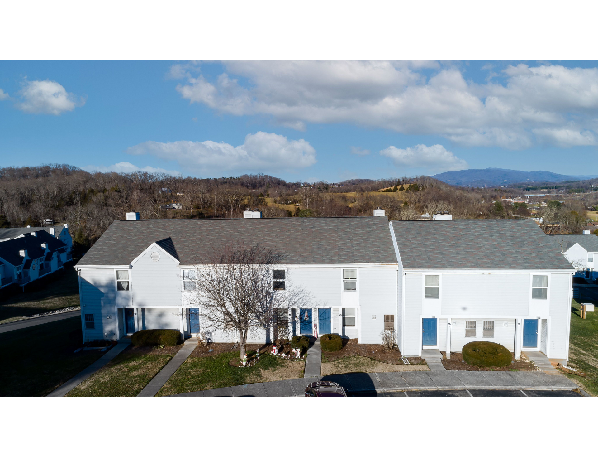 White townhouse row with blue shutters under a sunny sky, with trees and hills in the background
