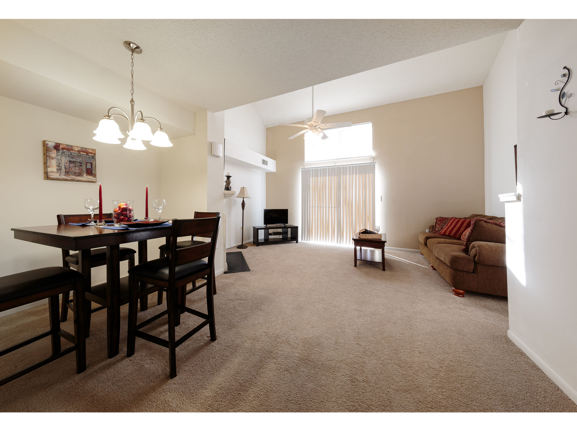 Open dining and living room with beige carpet, dark dining table, and bright windowed sitting area.