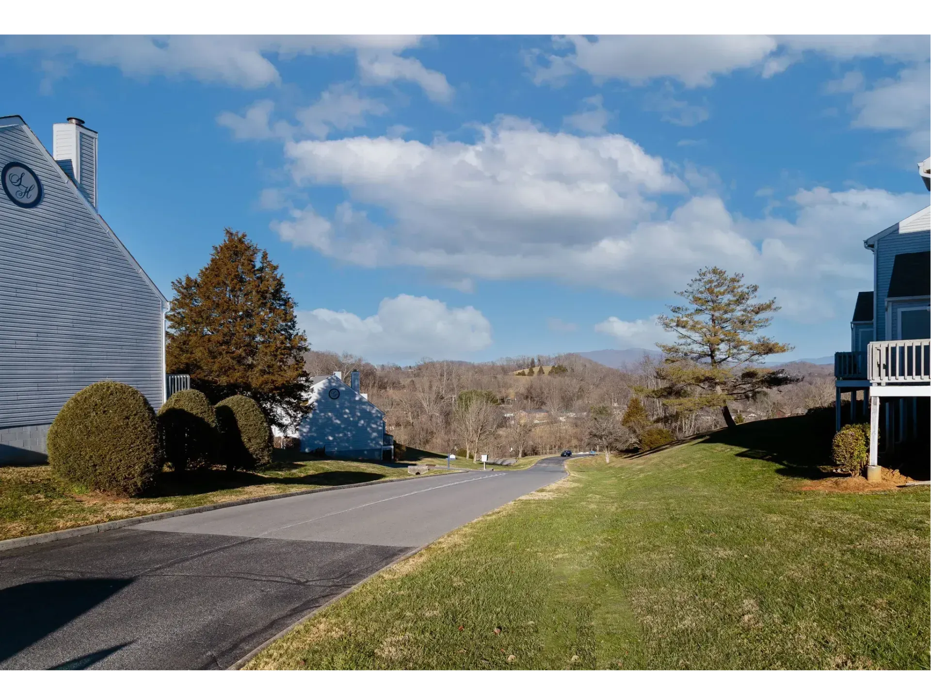 Suburban street with a sidewalk, grassy lawns, trees, and blue sky with clouds