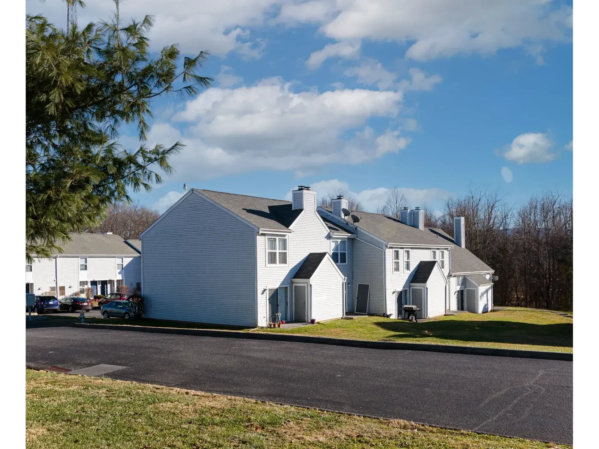 White colonial-style house with dormers and a dark roof beside a road under a blue sky