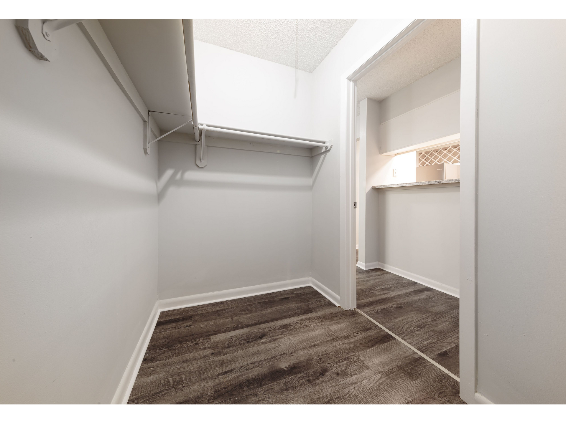 Empty walk-in closet with white walls, hanging rods, and dark wood-look flooring, viewed from the doorway