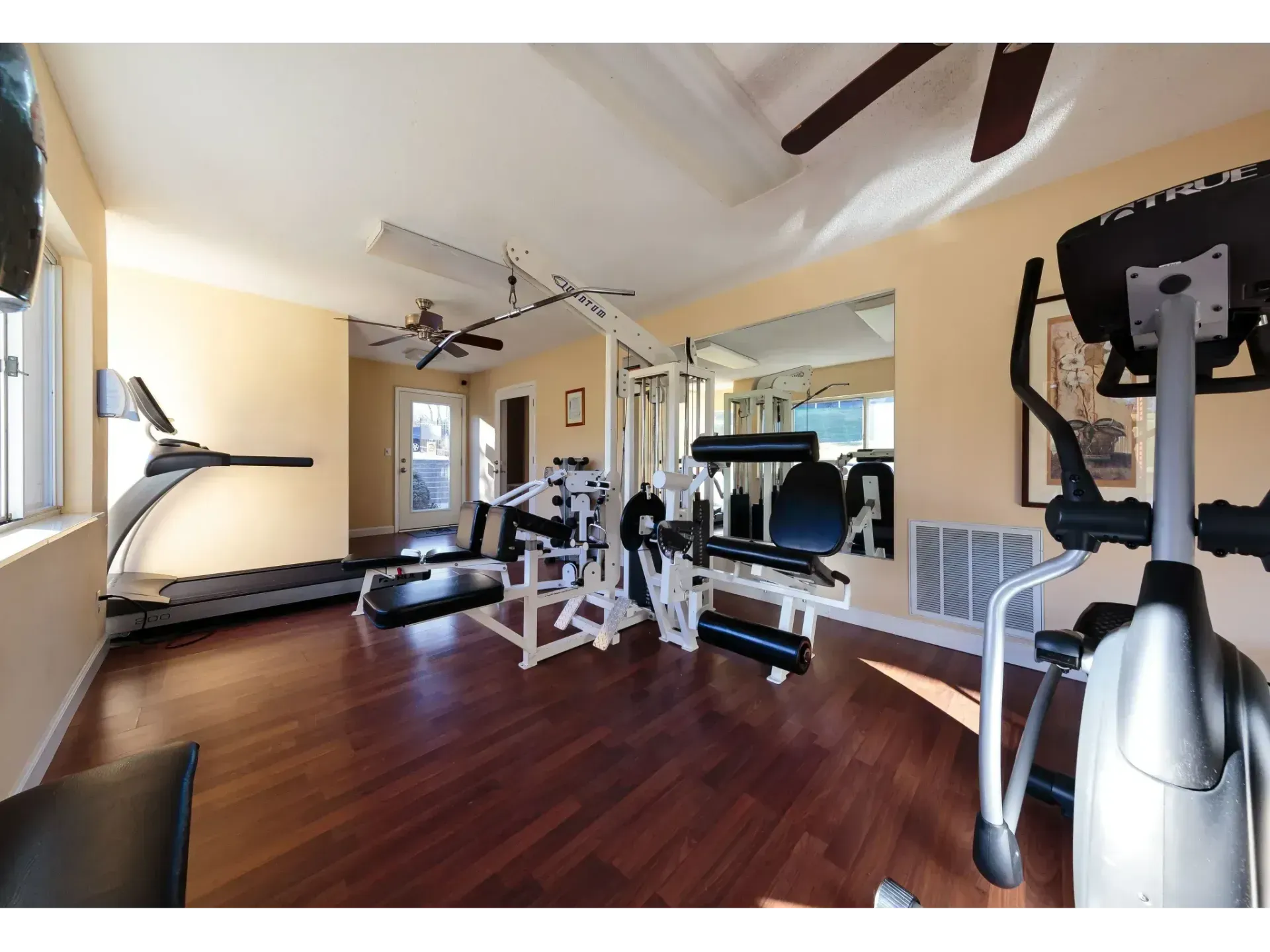 Home gym with treadmill, elliptical, weight bench, and mirrors on wood floors