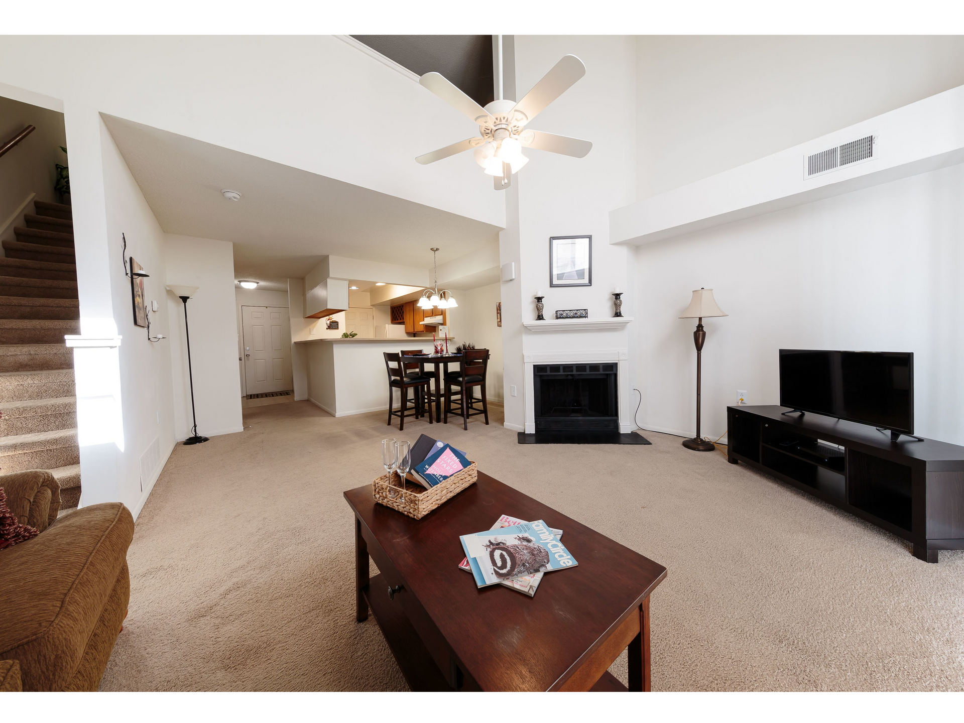 Bright living room with fireplace, TV, coffee table, ceiling fan, and open kitchen beyond