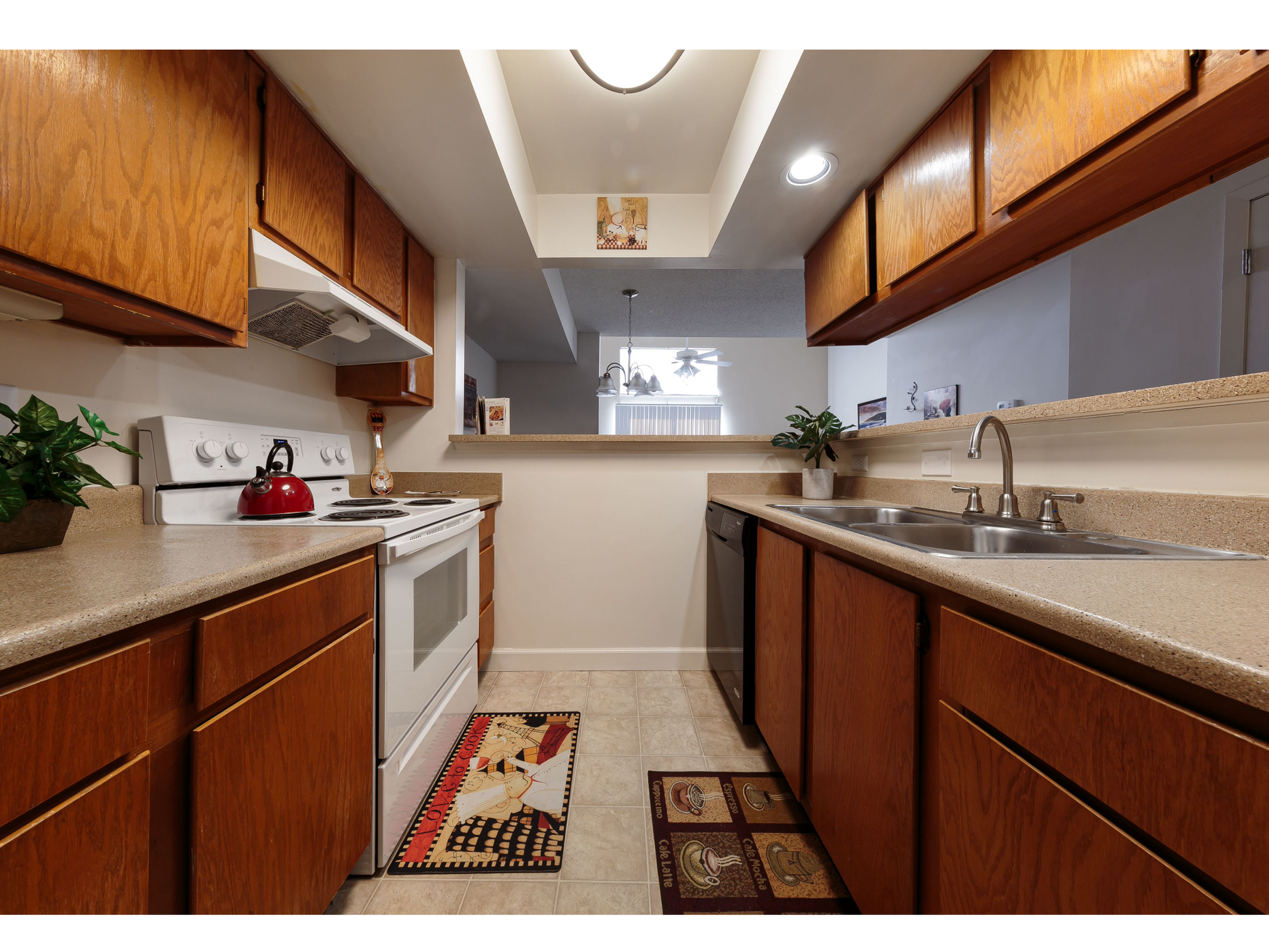 Narrow galley kitchen with wood cabinets, white appliances, beige countertops, and a small rug