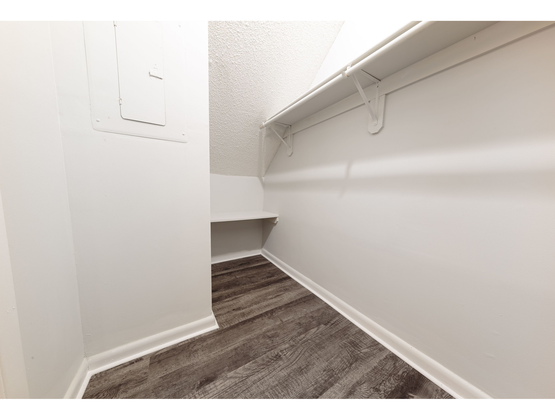 Empty walk-in closet with white walls, built-in shelf, and gray carpet flooring.