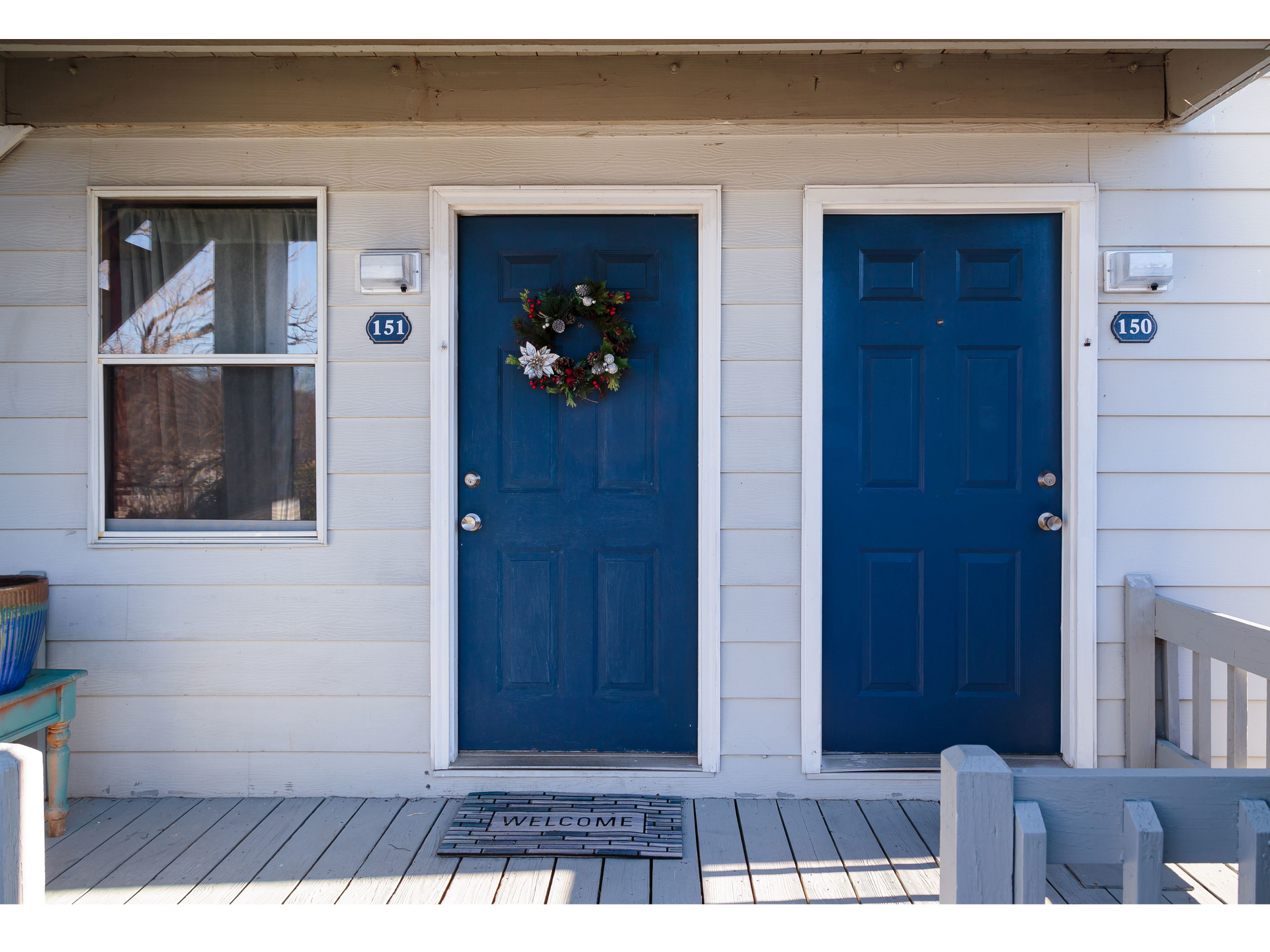 Front porch with two blue doors, a window, and a holiday wreath on one door.