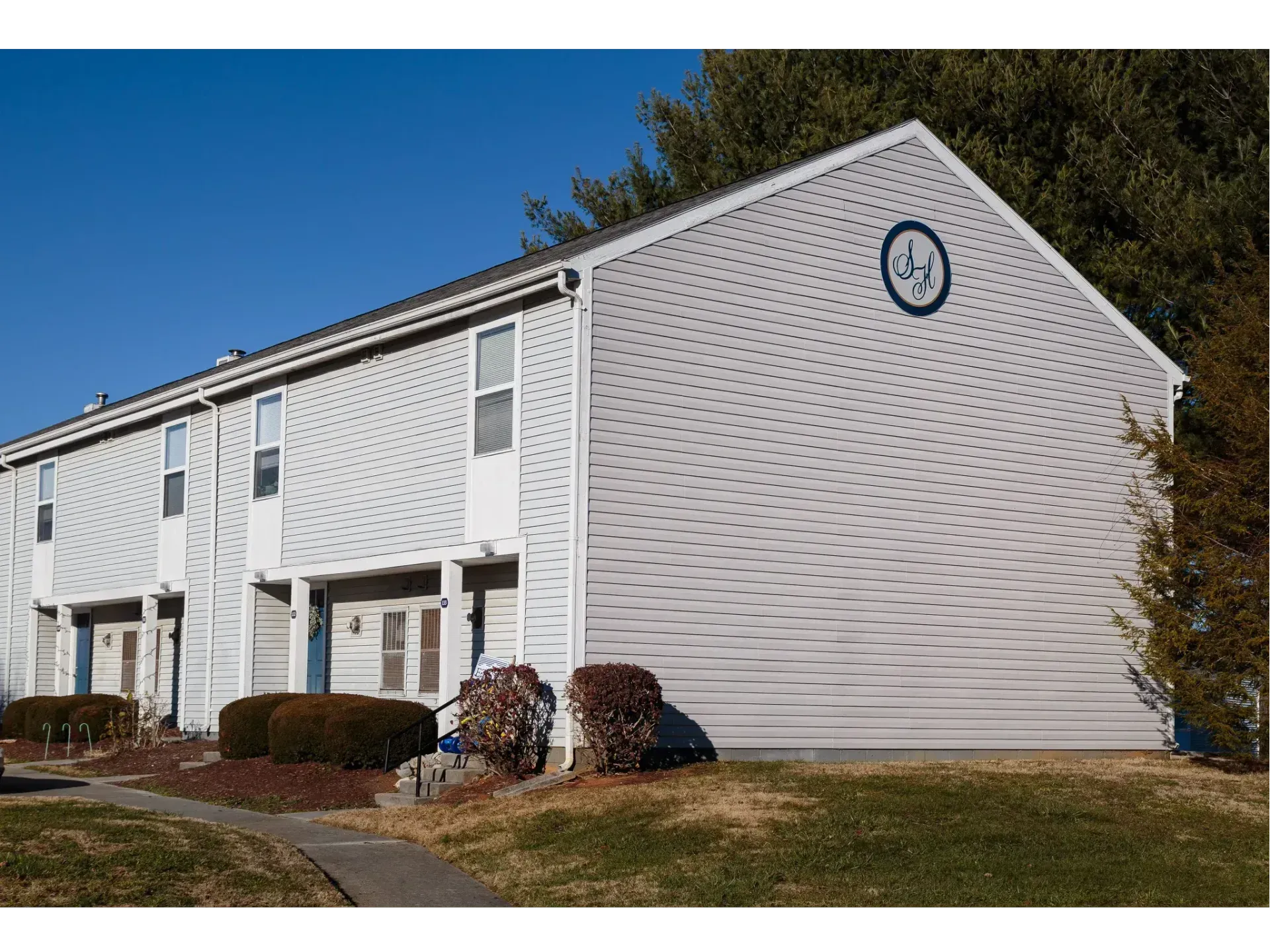 White apartment building with a clock on the side, front shrubs, and a clear blue sky