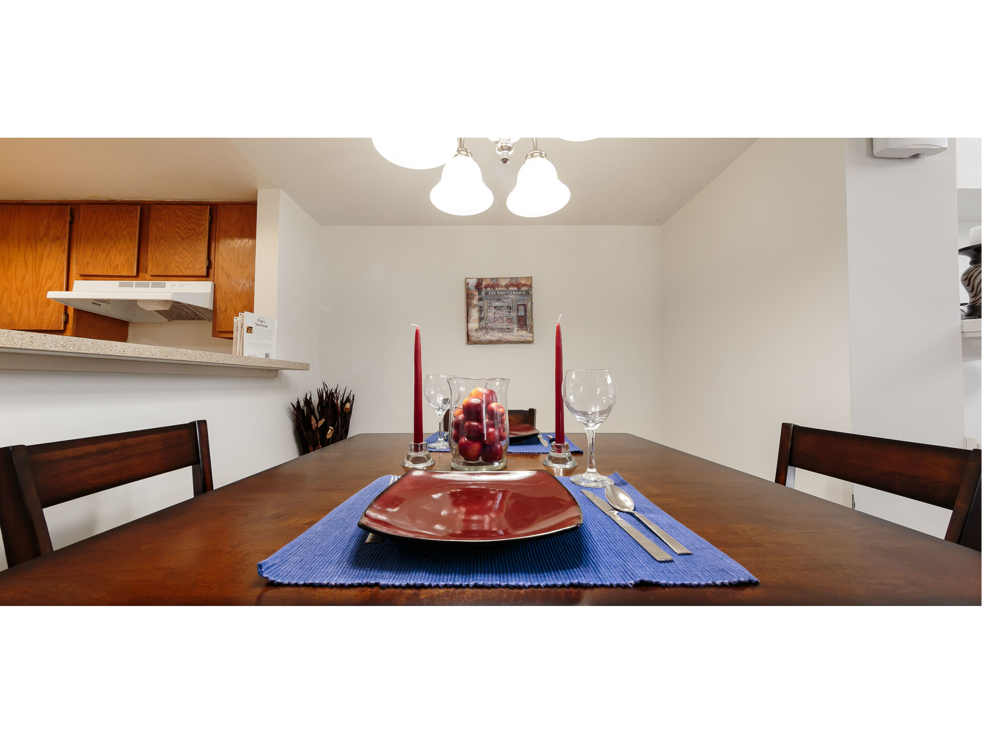 Dining room table set with red plates, blue placemat, candles, and chairs under a ceiling light.