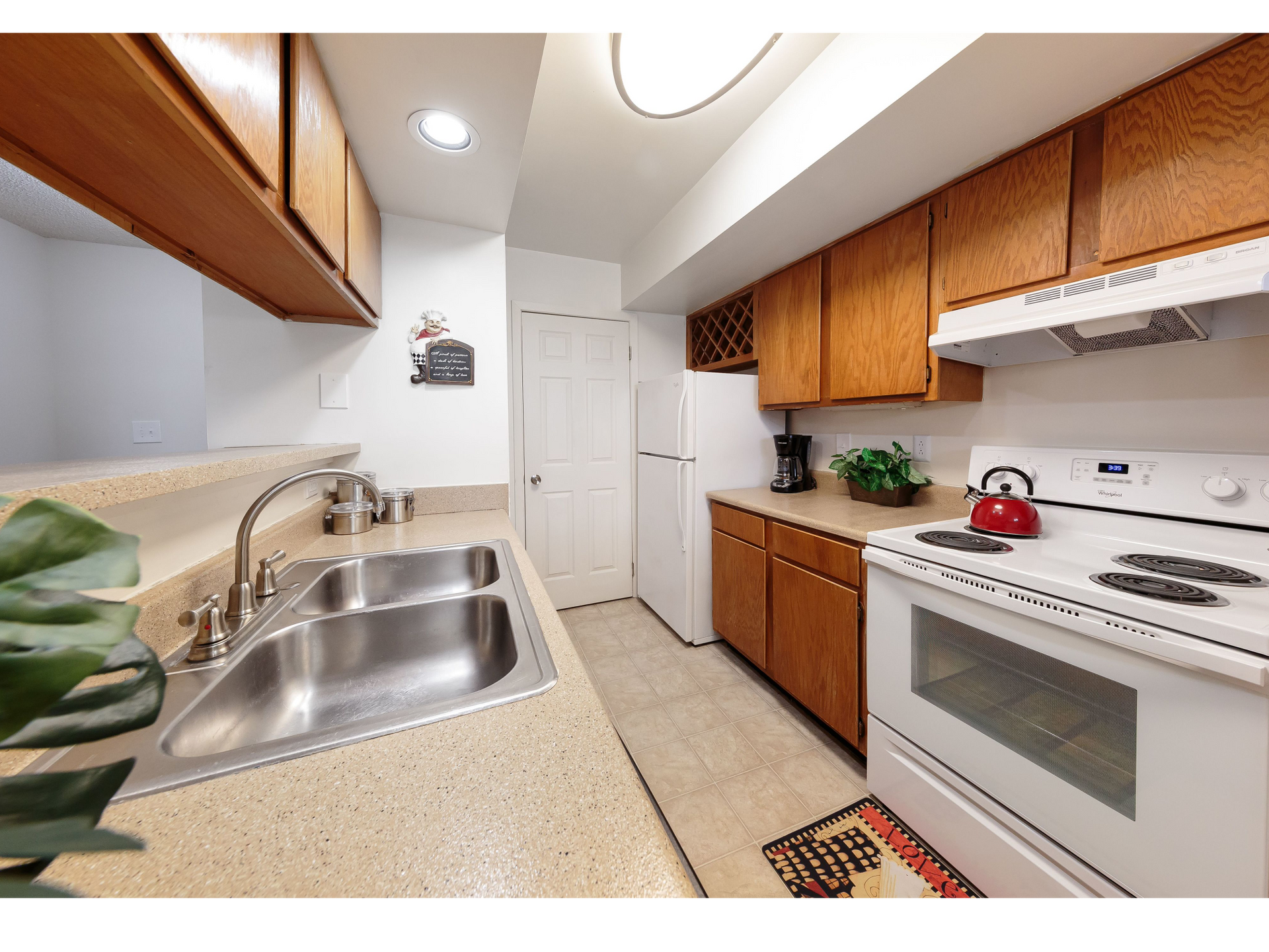 Small kitchen with wood cabinets, white appliances, sink, and beige countertops.