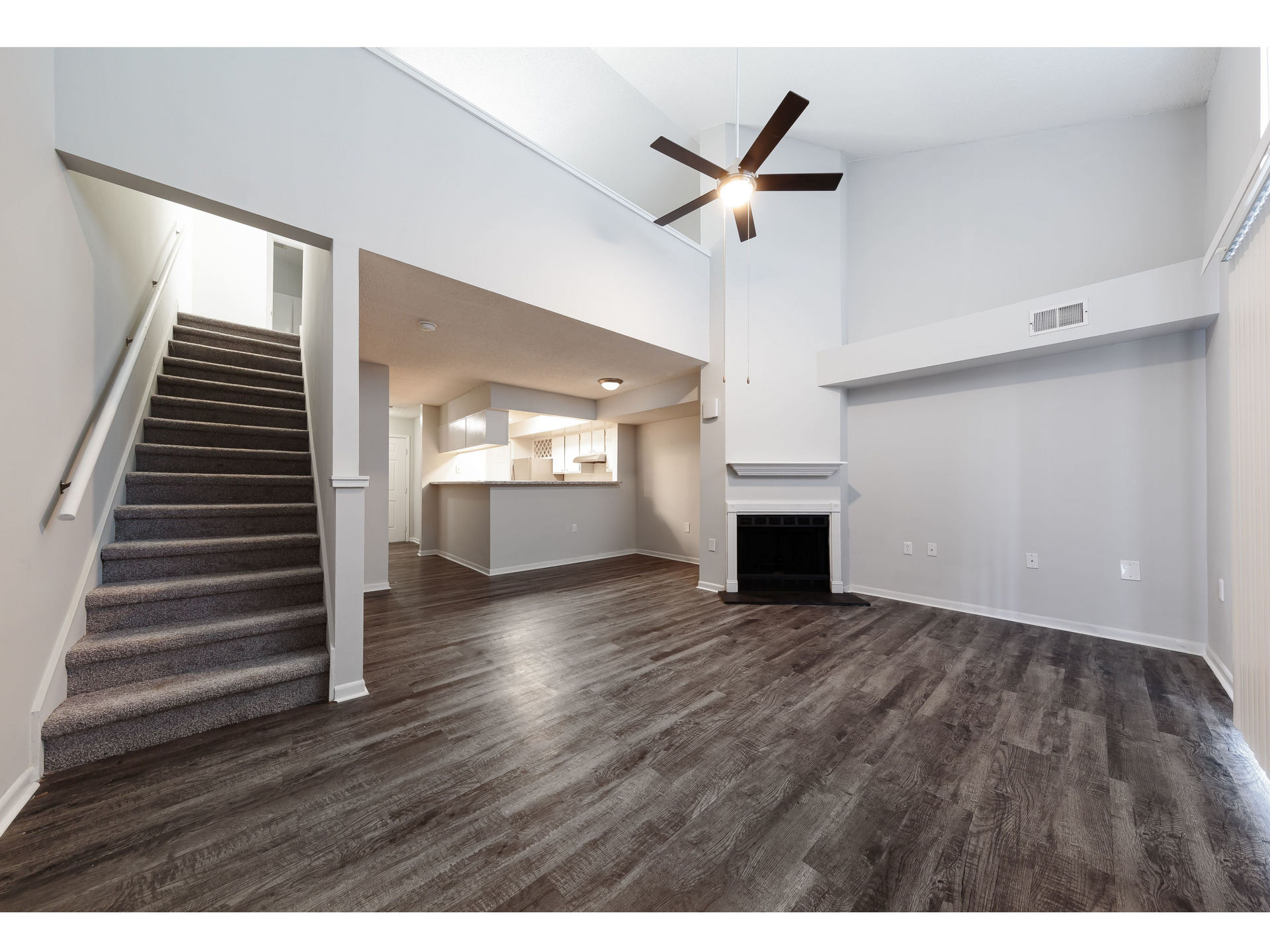 Empty modern living room with dark wood floors, staircase, ceiling fan, and fireplace.