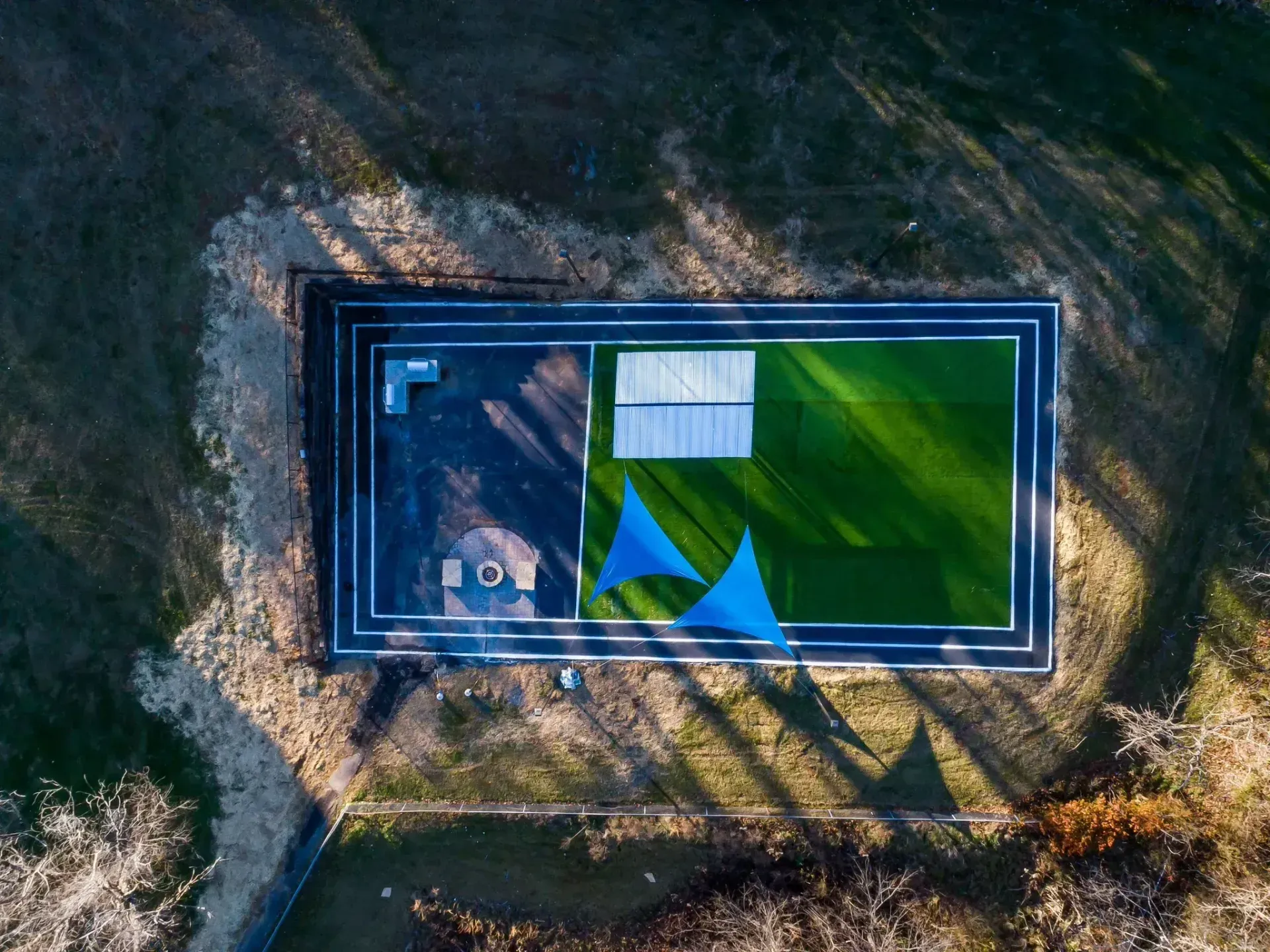 Aerial view of a small rectangular building with a green roof and surrounding dirt and grass.