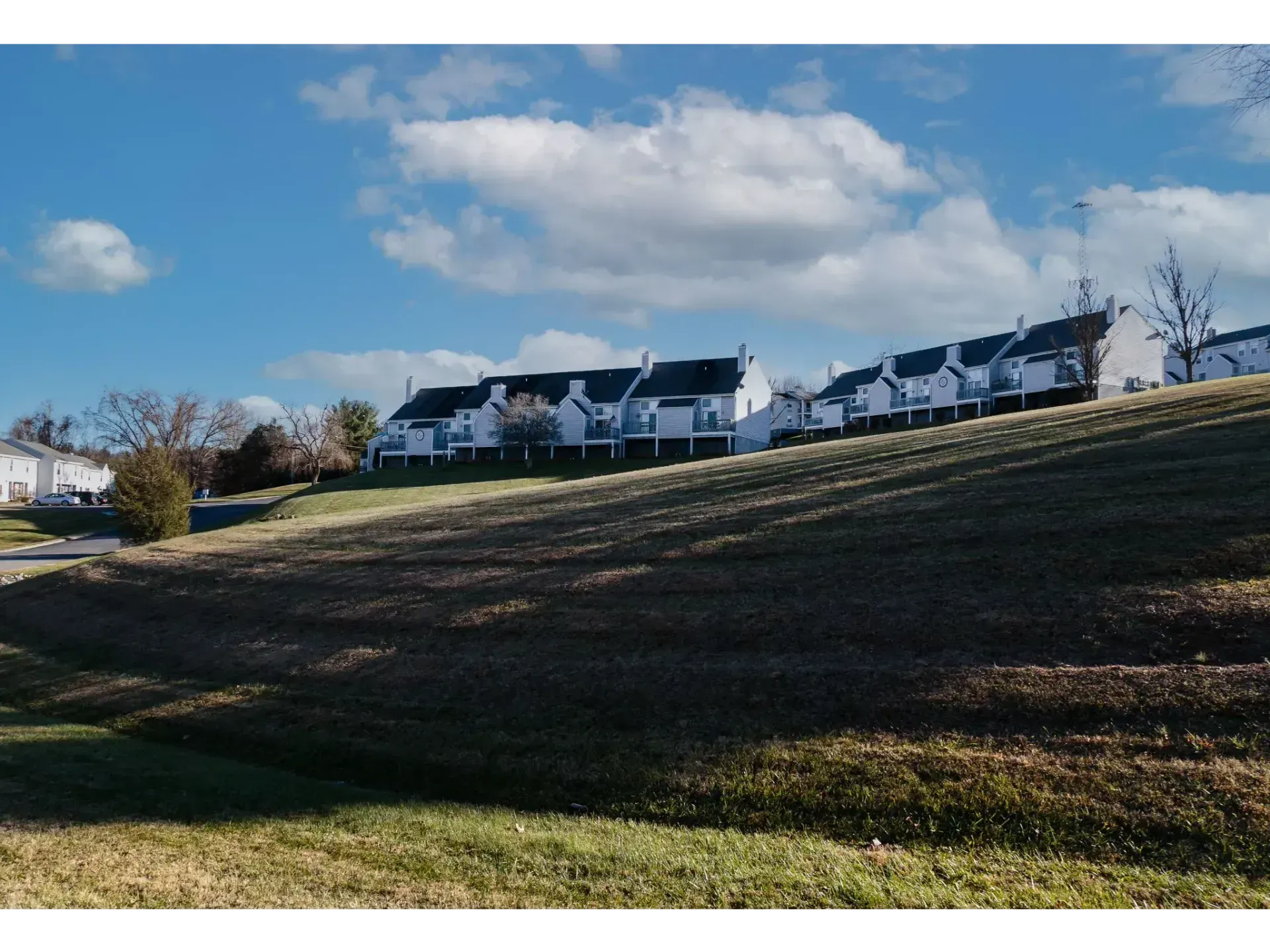Row of white houses on a grassy hillside under a blue sky with scattered clouds