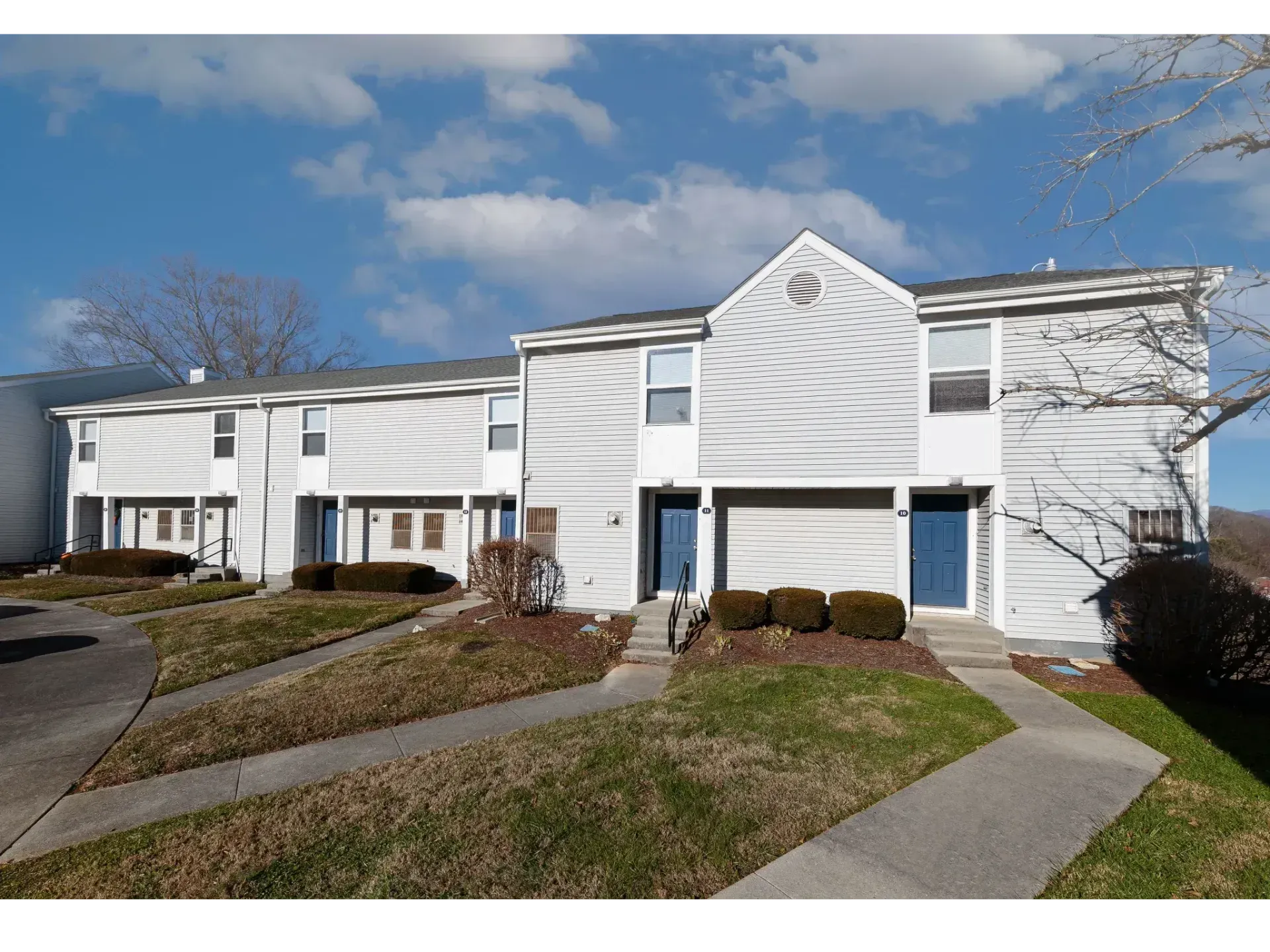 Row of white townhouses with garages and a sidewalk under a blue, partly cloudy sky