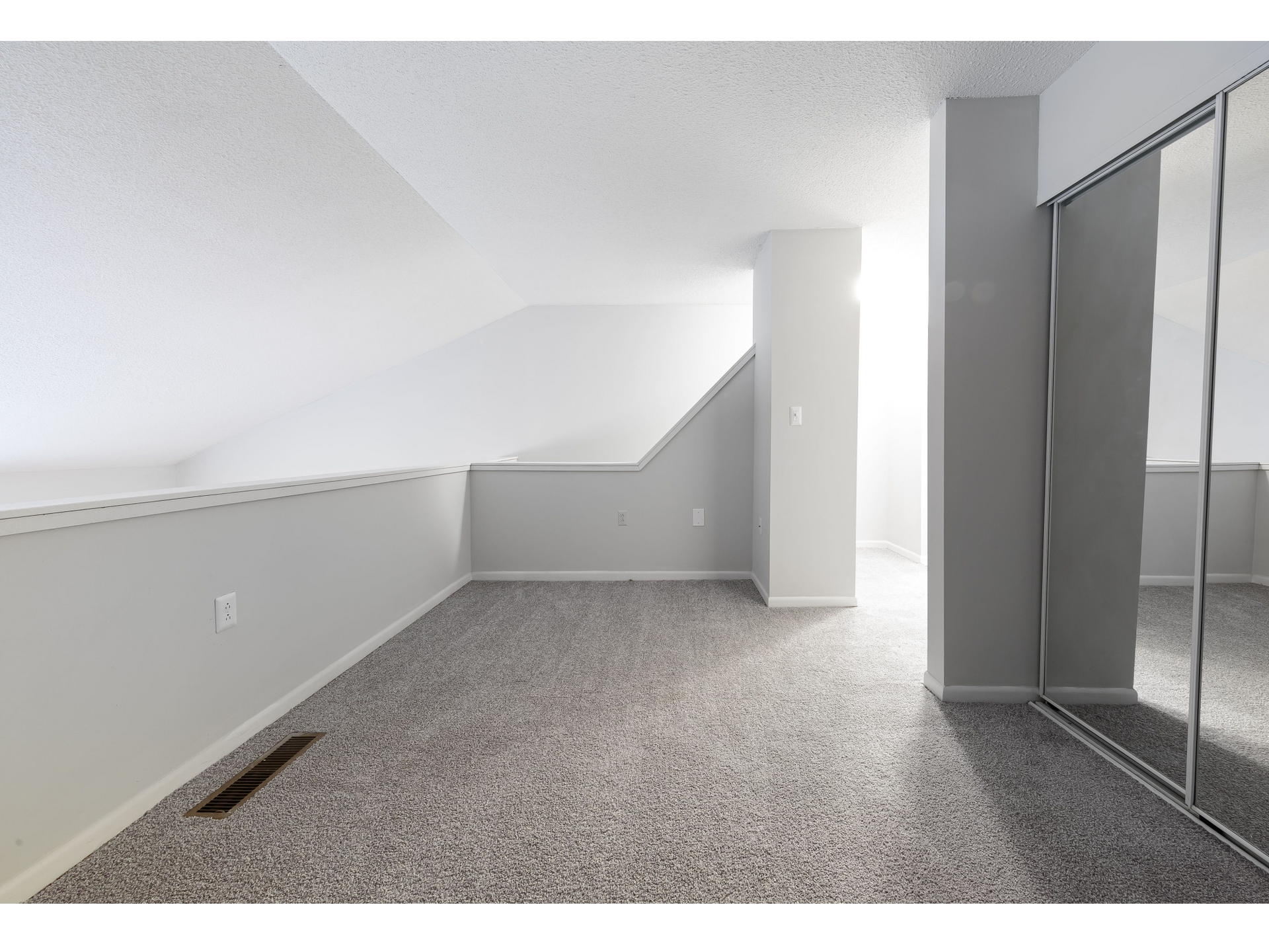 Empty carpeted attic room with sloped ceiling, skylight, and mirrored closet doors
