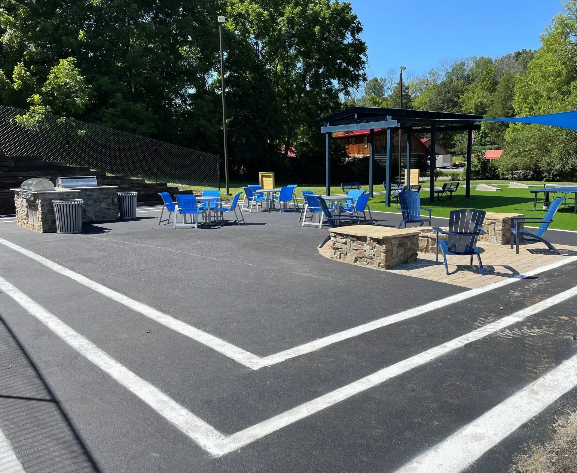 Outdoor picnic area with blue chairs, stone tables, and a shaded pavilion on a sunny day.