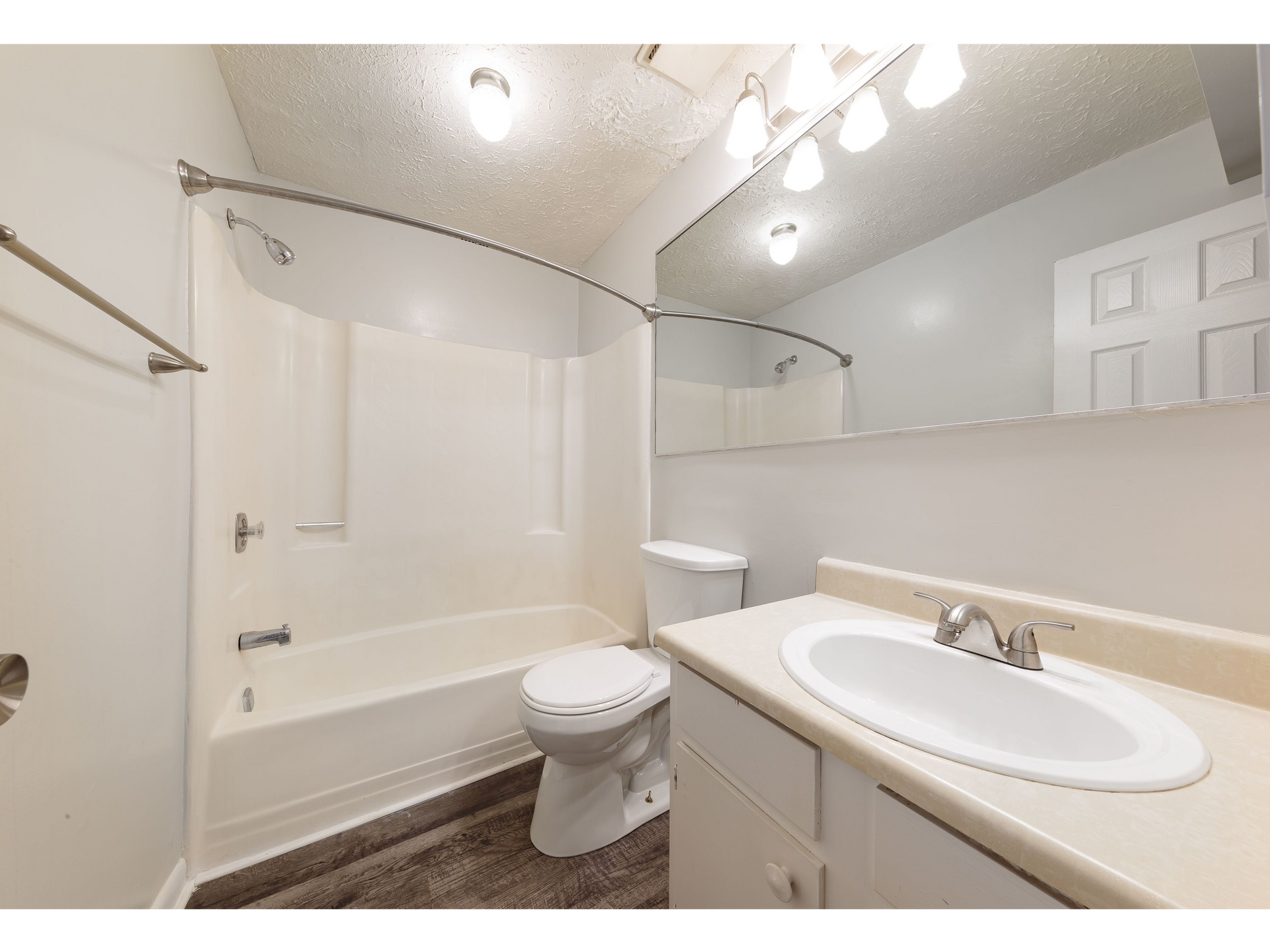 Bright bathroom with a bathtub, toilet, vanity sink, and large mirror
