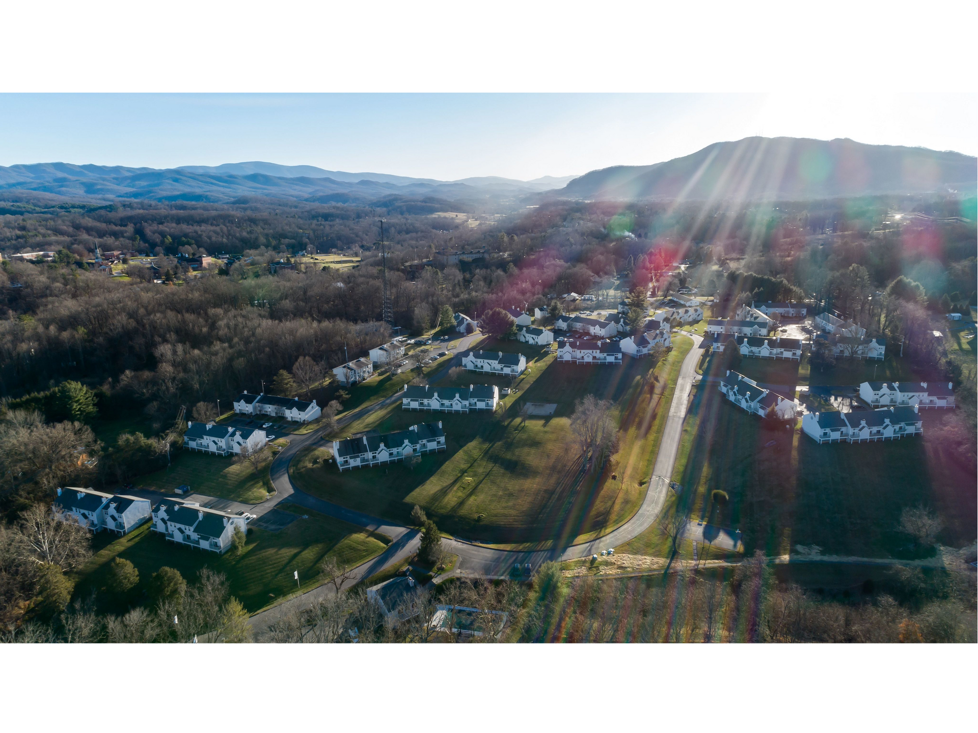 Aerial view of a suburban neighborhood with sunbeams over houses, roads, and distant hills