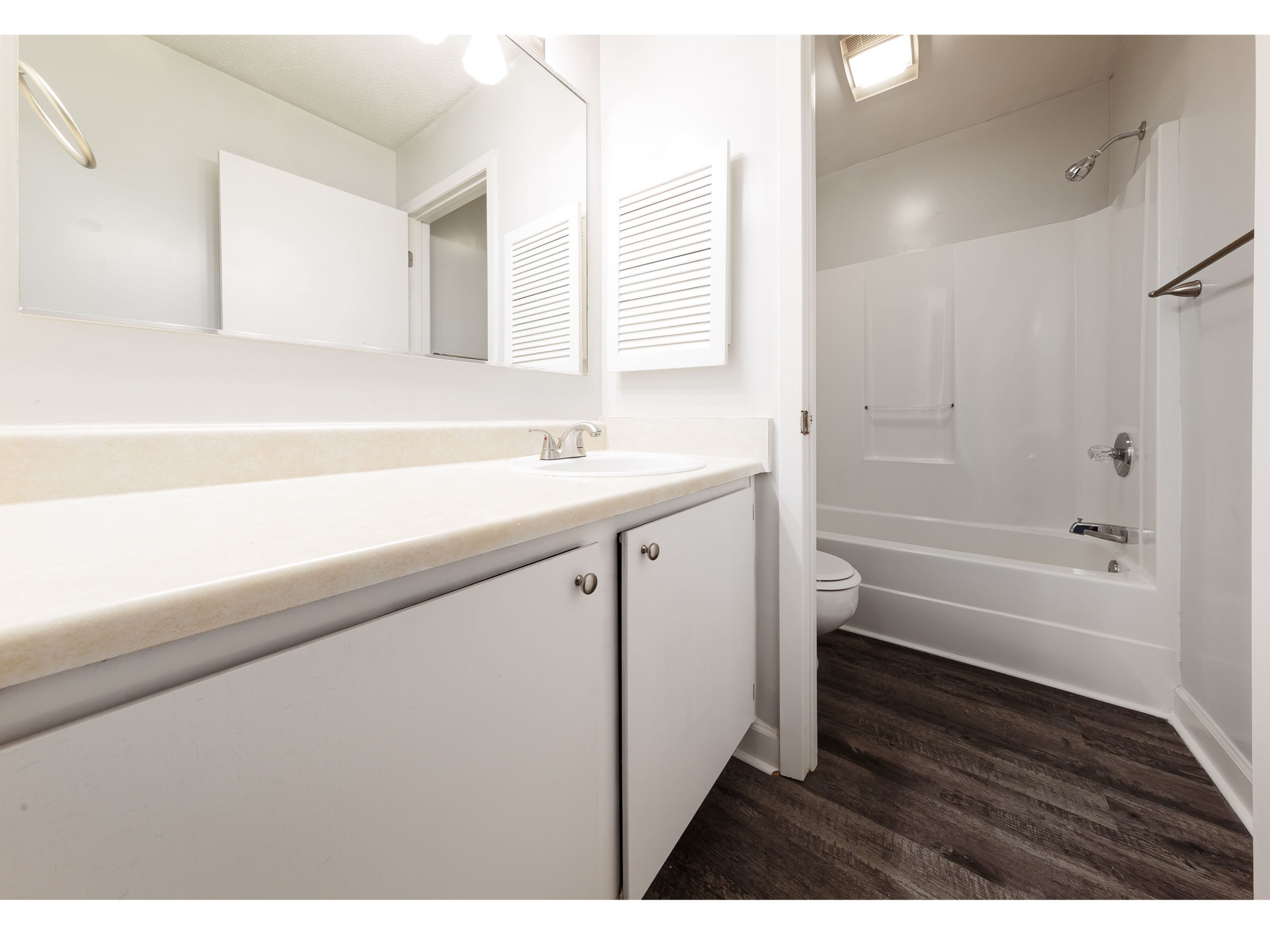 Modern white bathroom vanity and mirror beside a shower with dark wood-look flooring