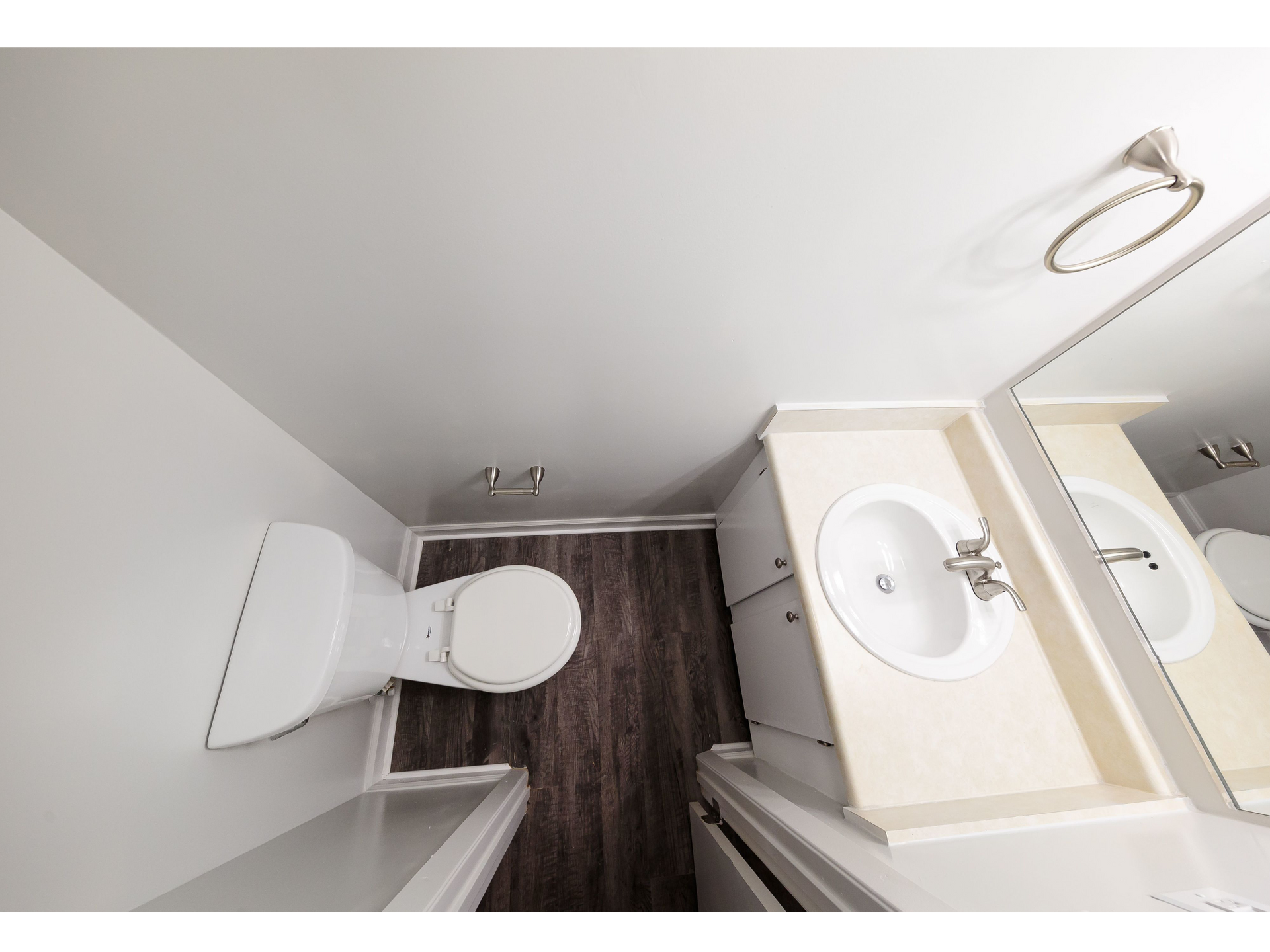 Small bathroom with toilet, sink vanity, and shower curtain on dark wood-look floor.