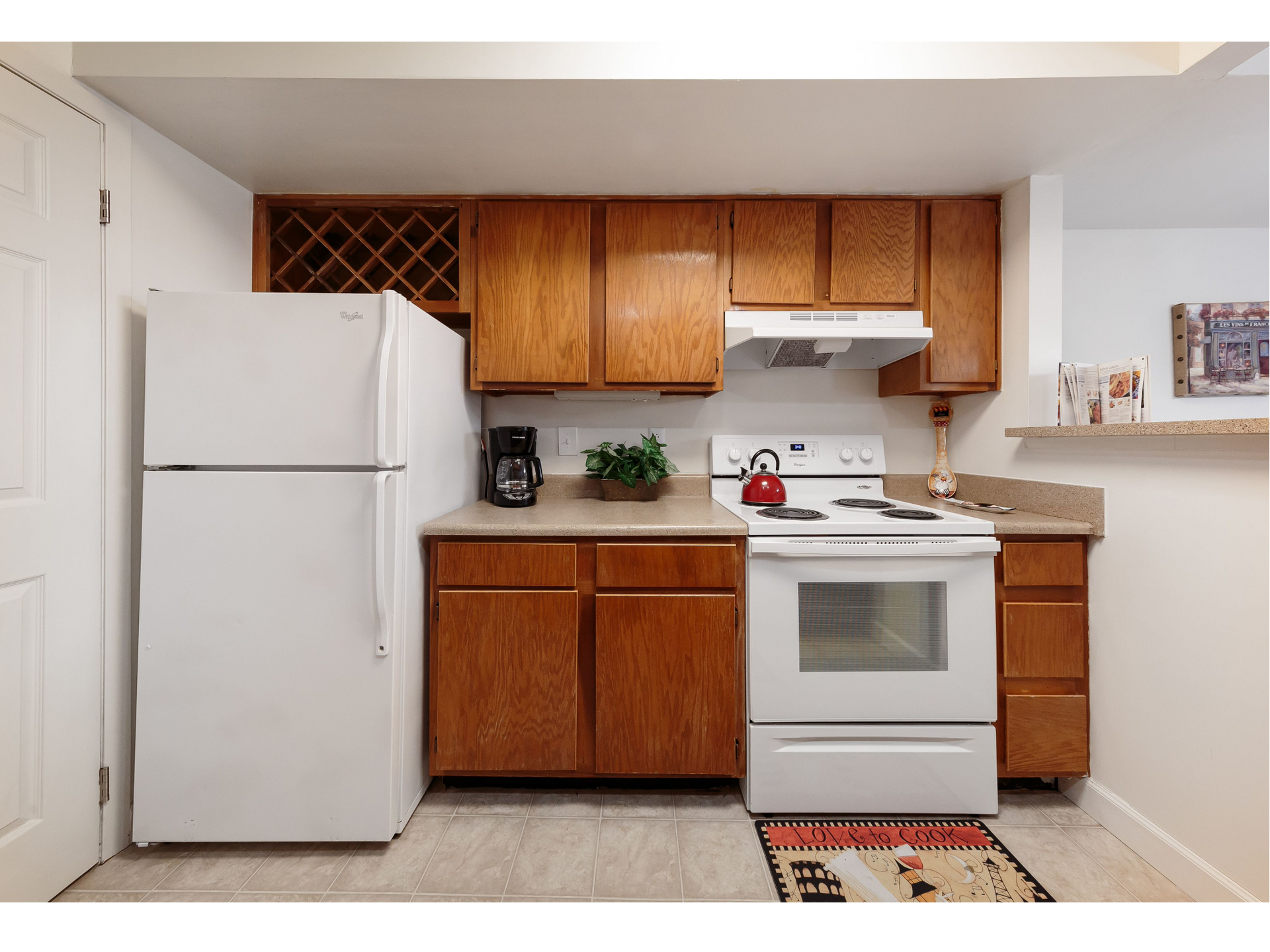 Small kitchen with white fridge and stove, wood cabinets, white countertops, and a wine rack.