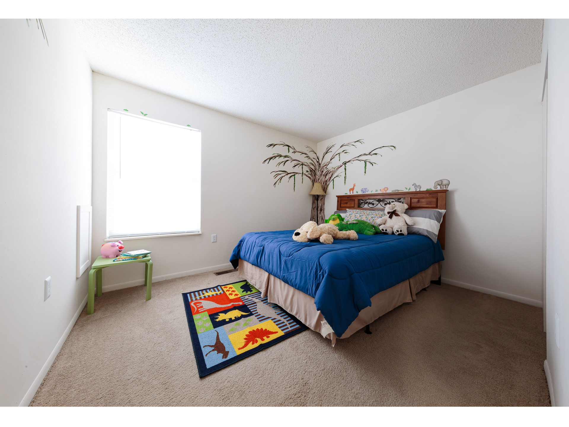 Bright bedroom with blue bedspread, colorful rug, window, and a small green chair.
