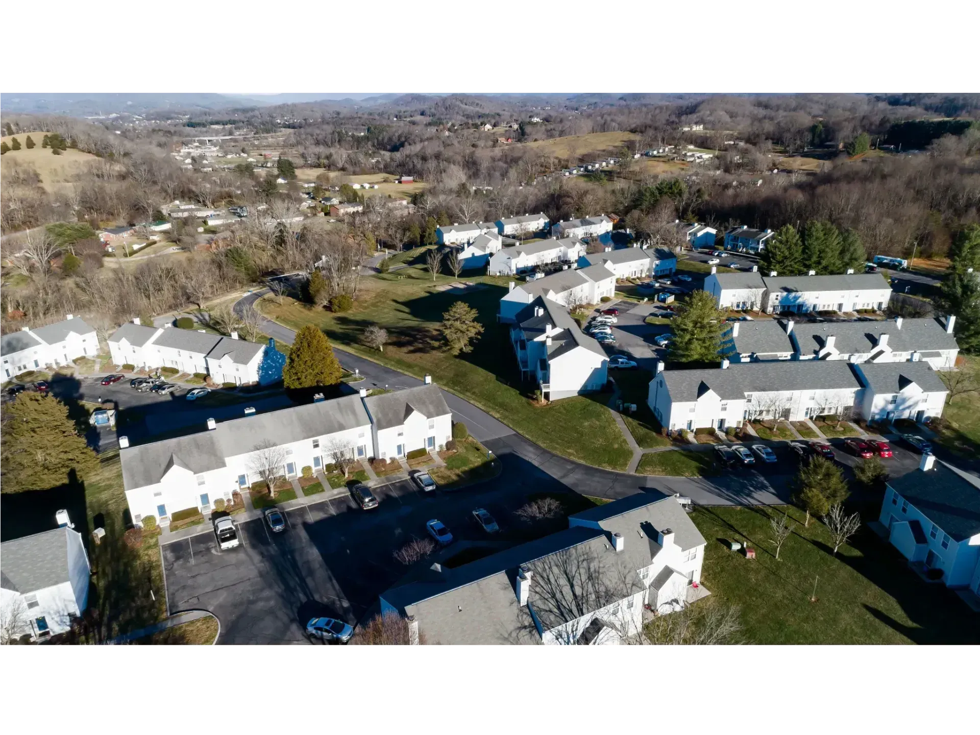 Aerial view of a suburban neighborhood with rows of white townhouses and parked cars on a sunny day