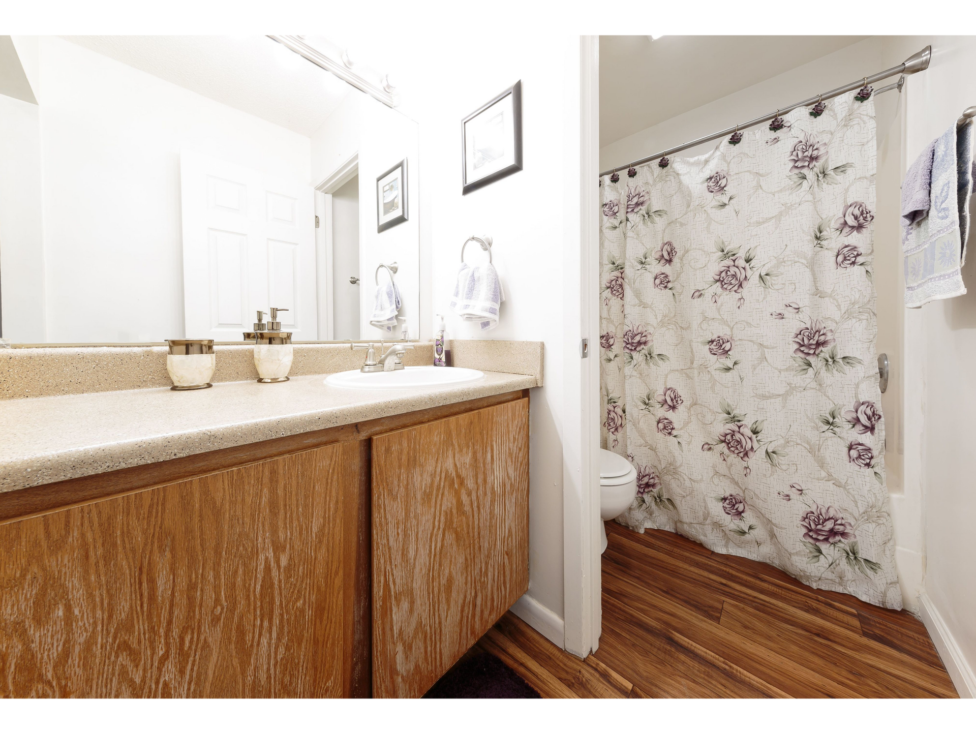 Bright bathroom vanity with large mirror and floral shower curtain on the right.