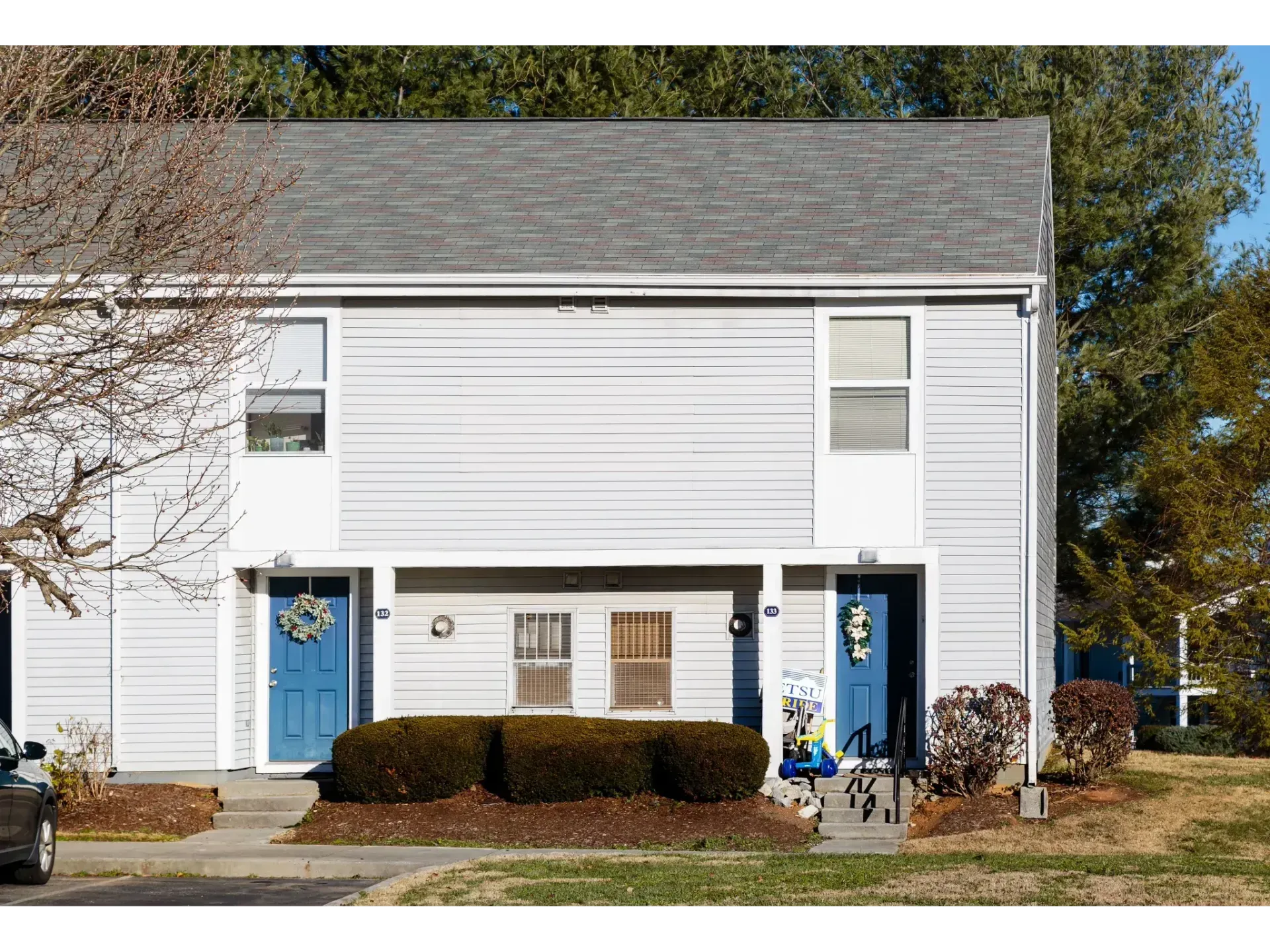 Two-story white townhouse with blue doors, trimmed bushes, and a front porch