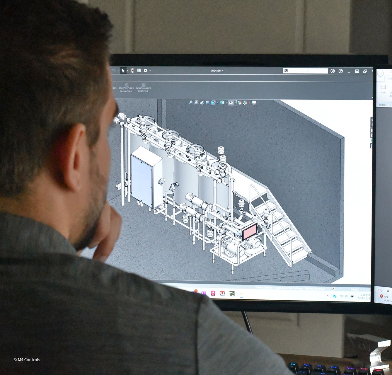 Man looking at a computer screen displaying a 3D model of industrial equipment.