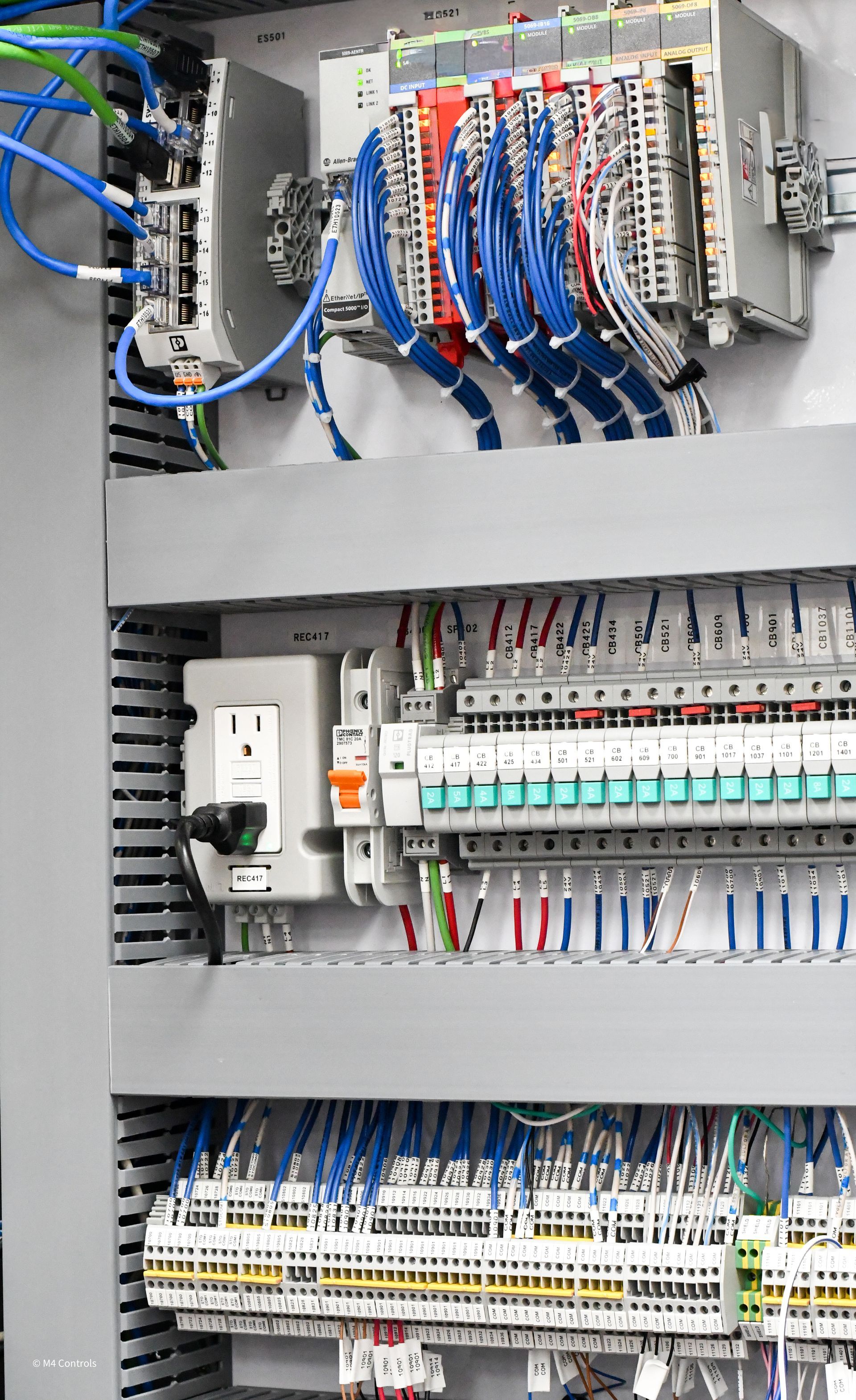 Electrical control panel with rows of terminals and wiring. Blue, black, and white cables are neatly arranged.