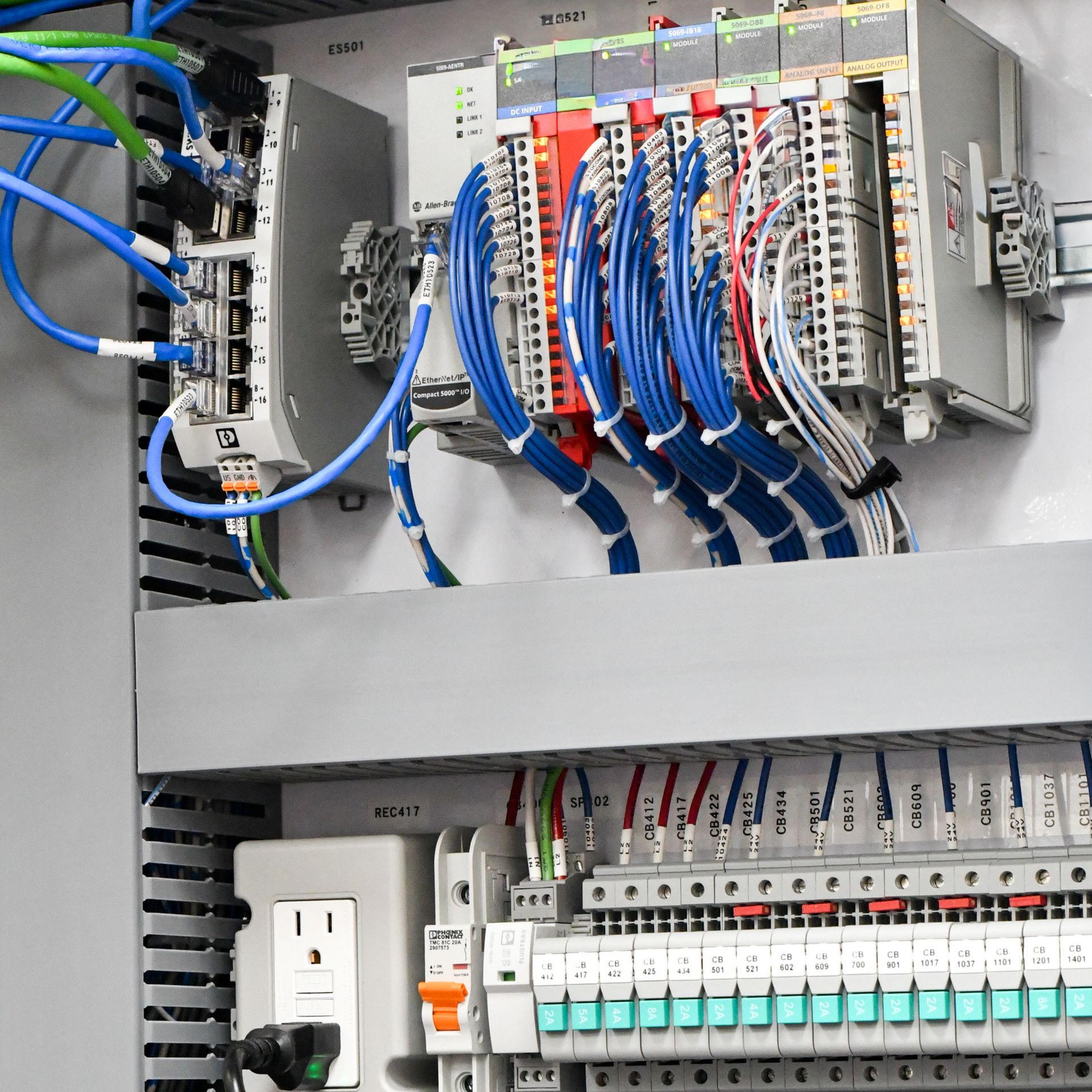 Control panel with wires, electrical components, power outlets, and a gray cabinet.