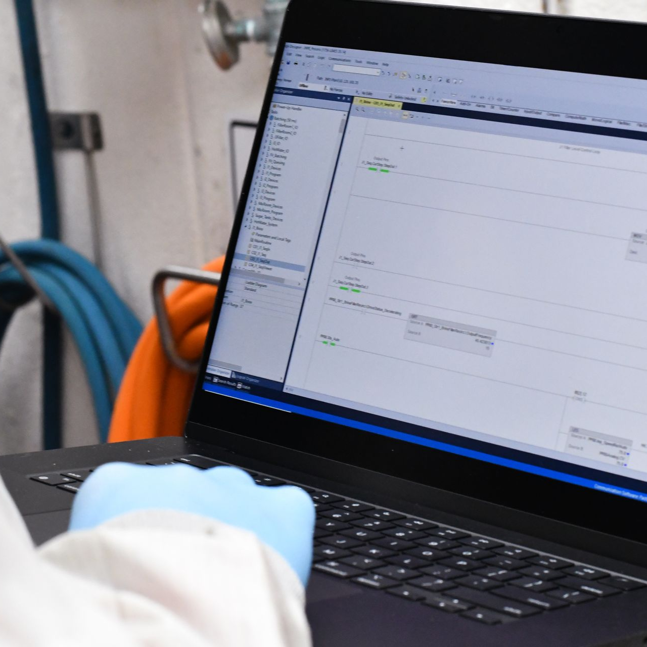Person wearing a blue glove using a laptop, possibly programming or analyzing data.
