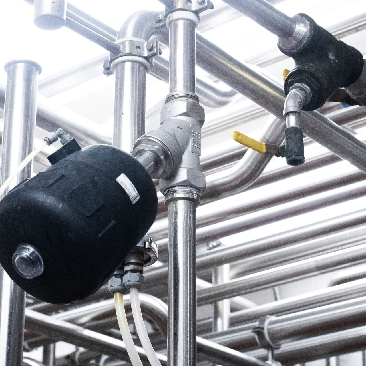 Shiny metal pipes, valves, and a black cylindrical component in an industrial setting.