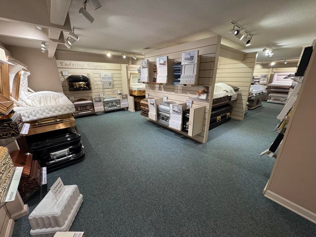 Carpeted showroom with stacked mattresses and bed frames in a warmly lit display area