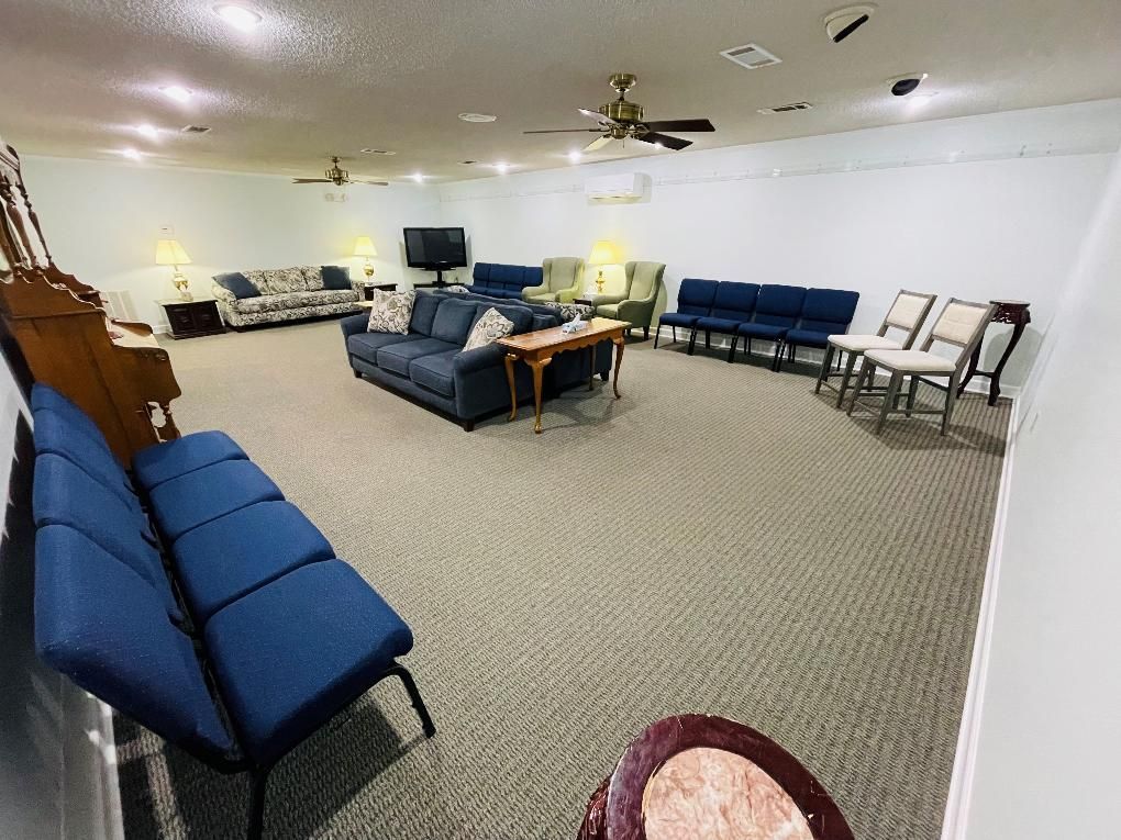 Spacious lounge with blue couches, chairs, tables, and carpeted floor under ceiling fans.