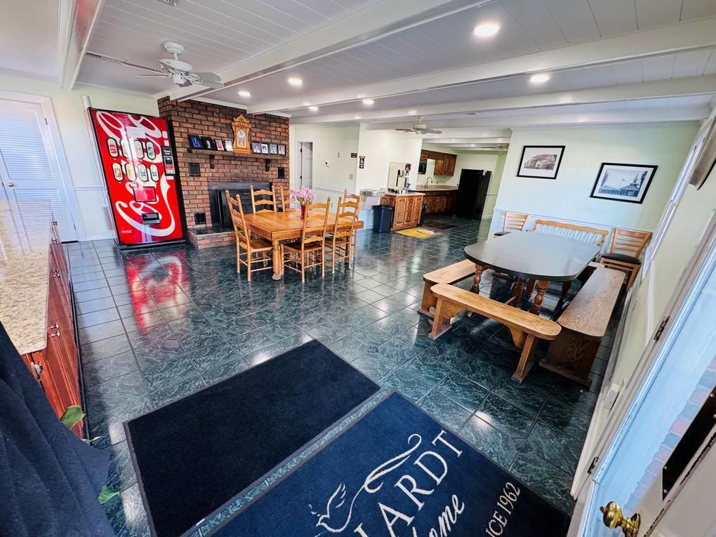 Brick-walled dining room with wooden tables, black tile floor, and red Coca-Cola vending machine