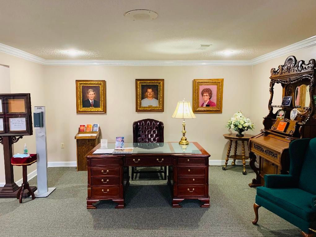 Office with wooden desk, framed portraits on the wall, and teal chairs in a formal waiting room