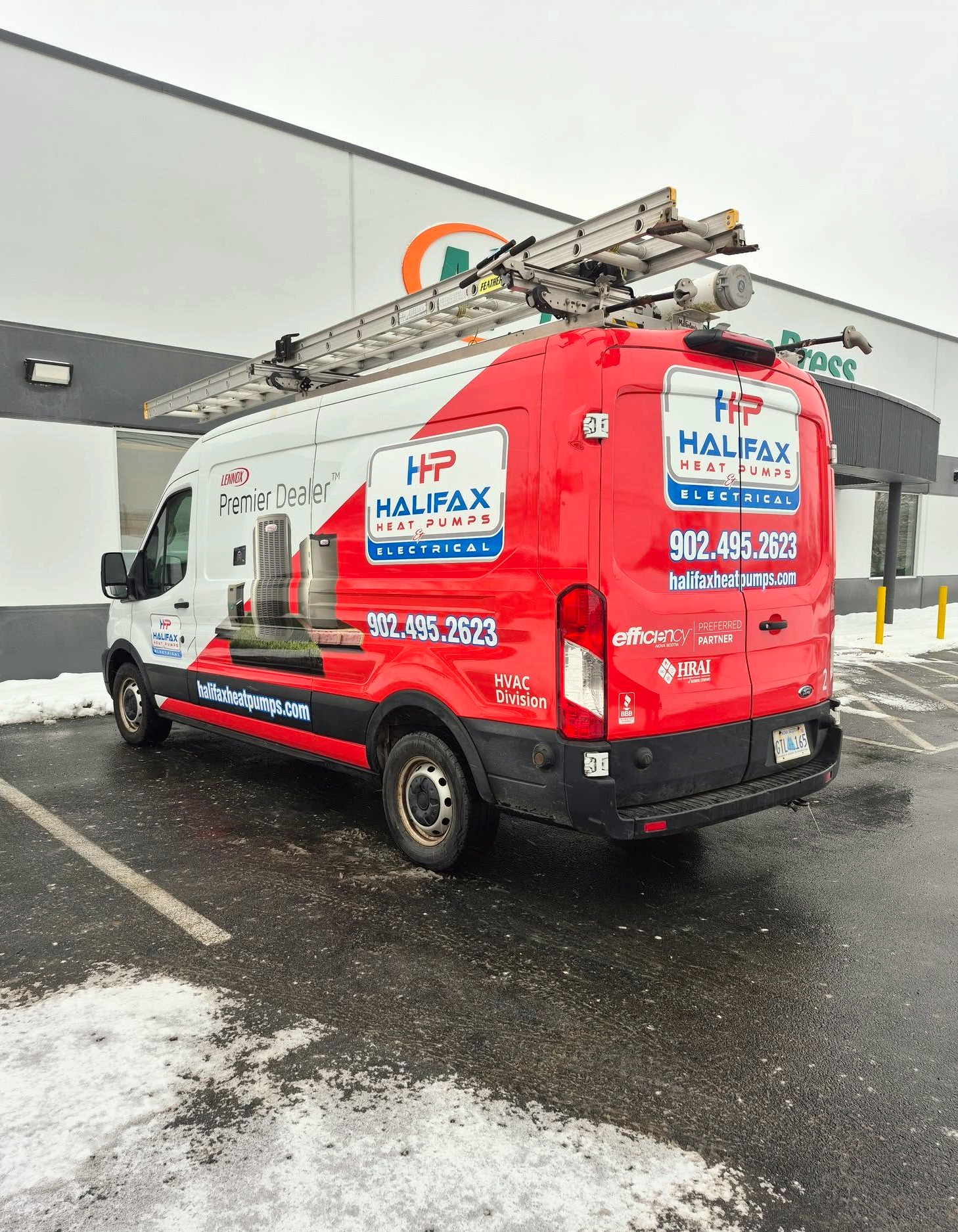 Red Halifax service van parked outside a building on a wet, snowy lot, with a ladder on top.
