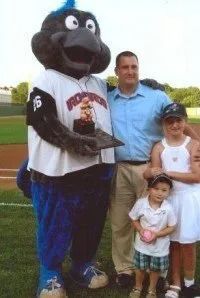 Baseball mascot holding trophy with a family on the field.