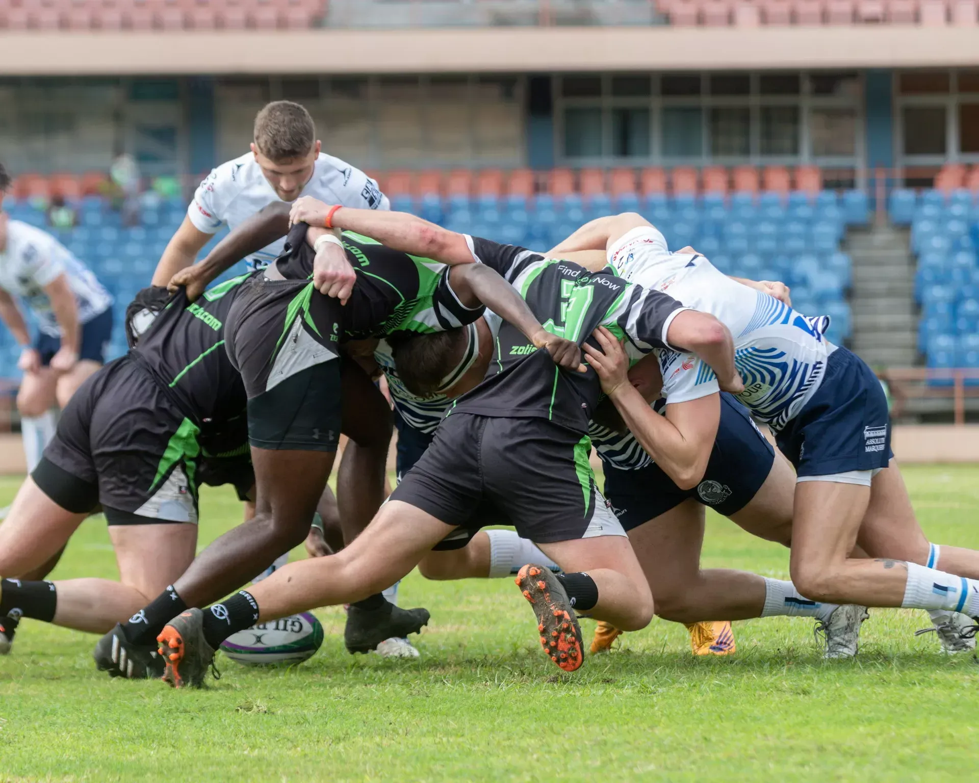 Rugby players in black and white kits भिडe in a scrum on a grassy field.