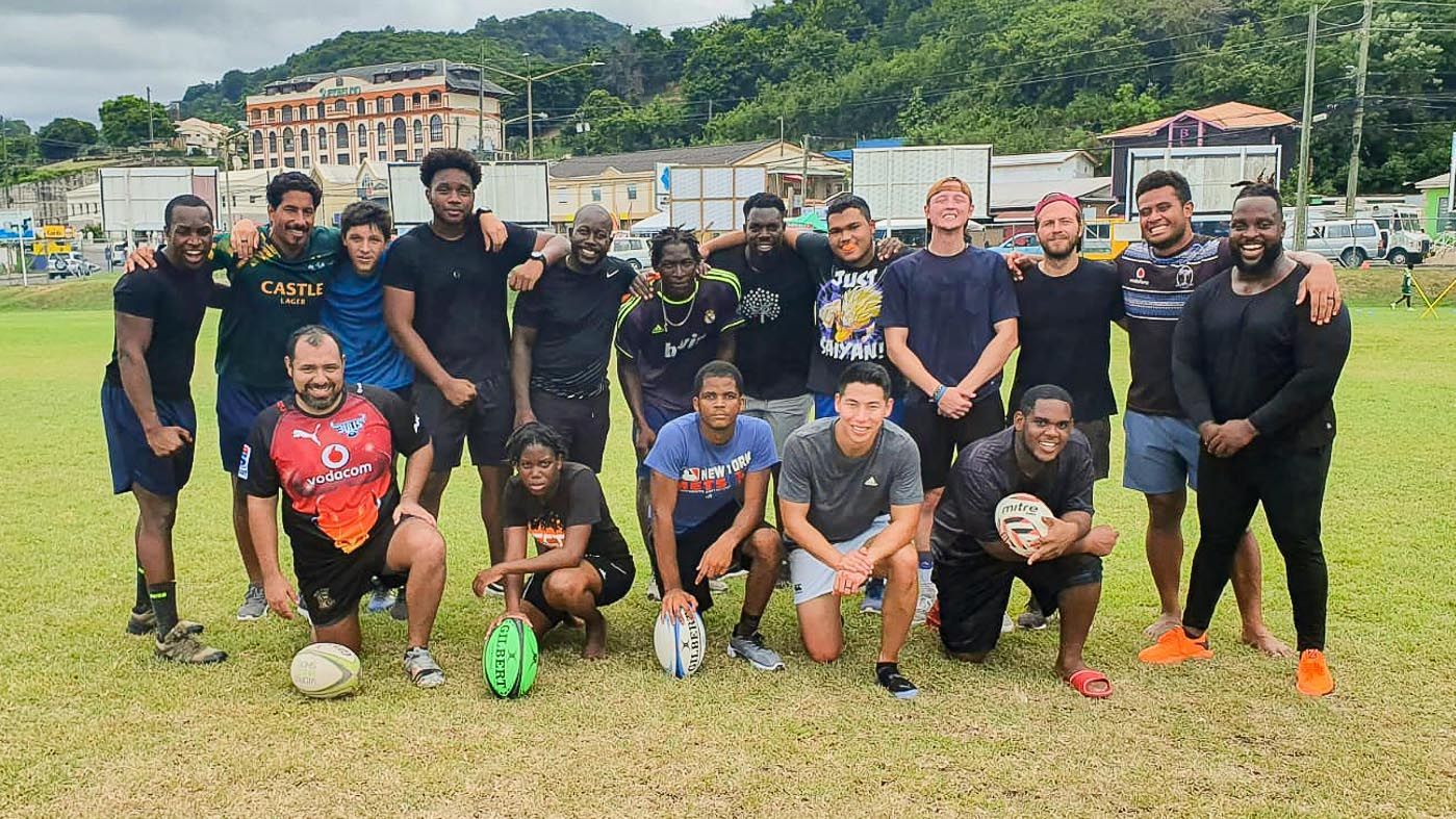 Soccer team posing on a grassy field with a ball, houses and hills in the background