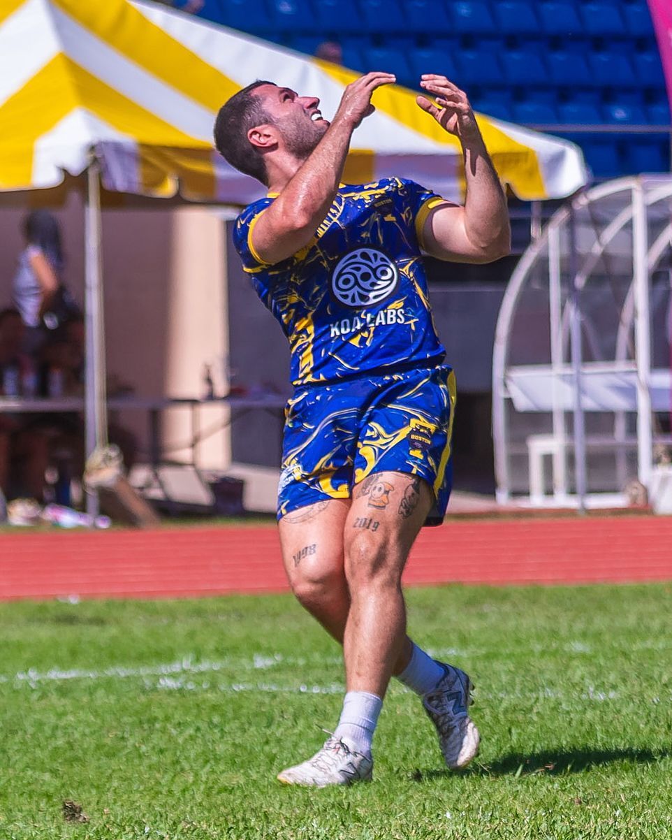 Athlete in blue and yellow uniform leaping to catch a ball on a sunny field
