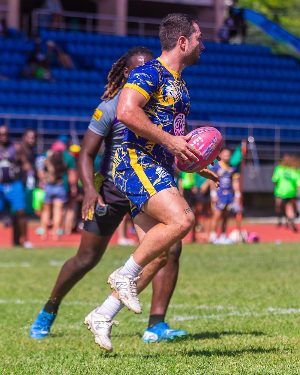 Rugby player in blue and yellow runs with the ball on a field during a match