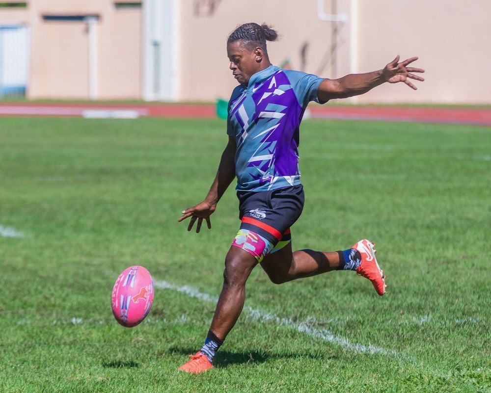 Soccer player in blue and purple kit kicking a pink ball on a green field