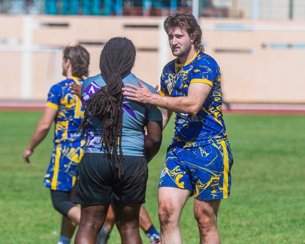 Rugby players in blue and yellow uniforms on a field, one speaking with a referee in black shorts.